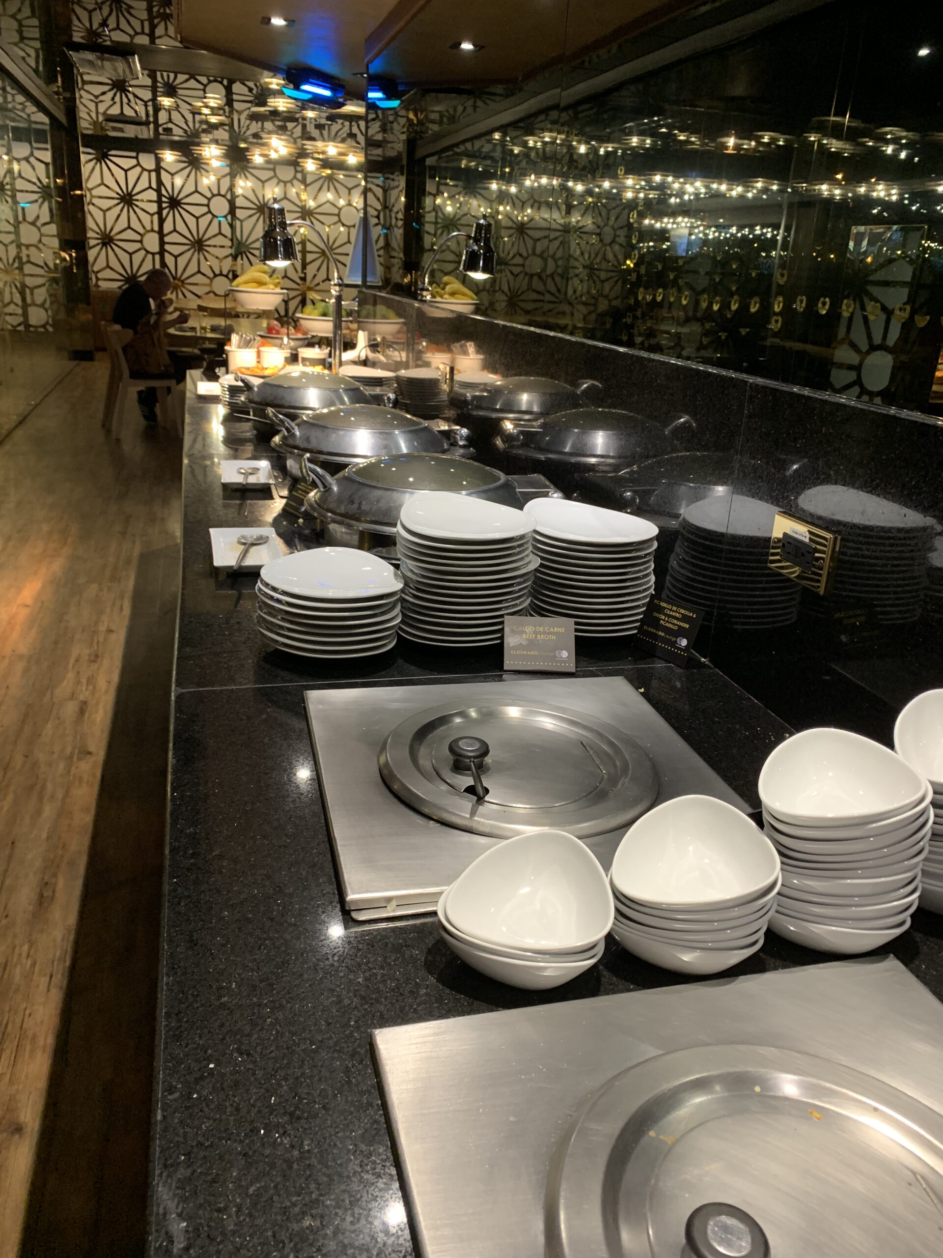 Buffettheke mit gestapelten Tellern, Schüsseln und Chafing Dishes auf schwarzer Granitfläche.