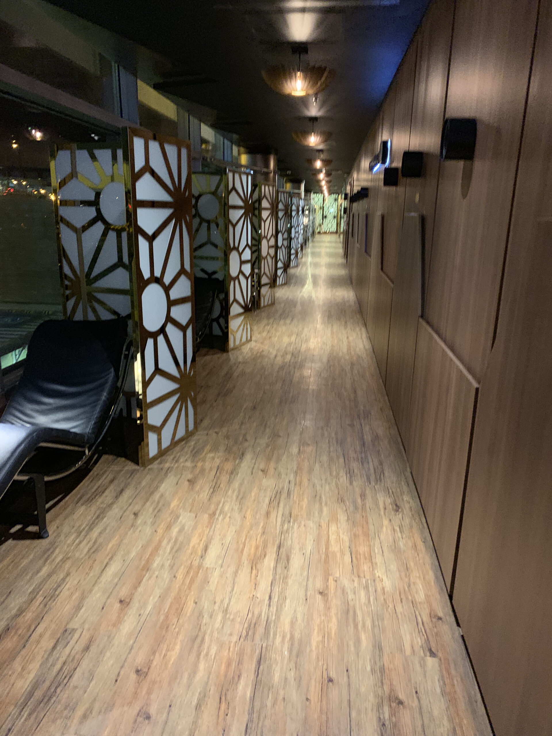 Langer Korridor mit Holzboden, dekorierten Trennwänden in Gold-Weiß und Holzverkleidung an der rechten Wand.