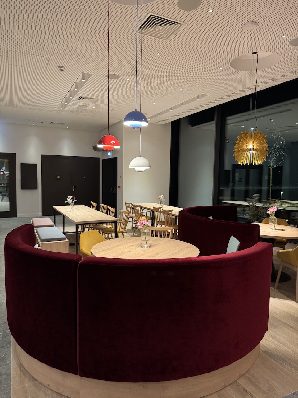 Rundsofa in Bordeauxrot mit rundem Holztisch im Frühstücksbereich, bunte Pendelleuchten an der Decke.