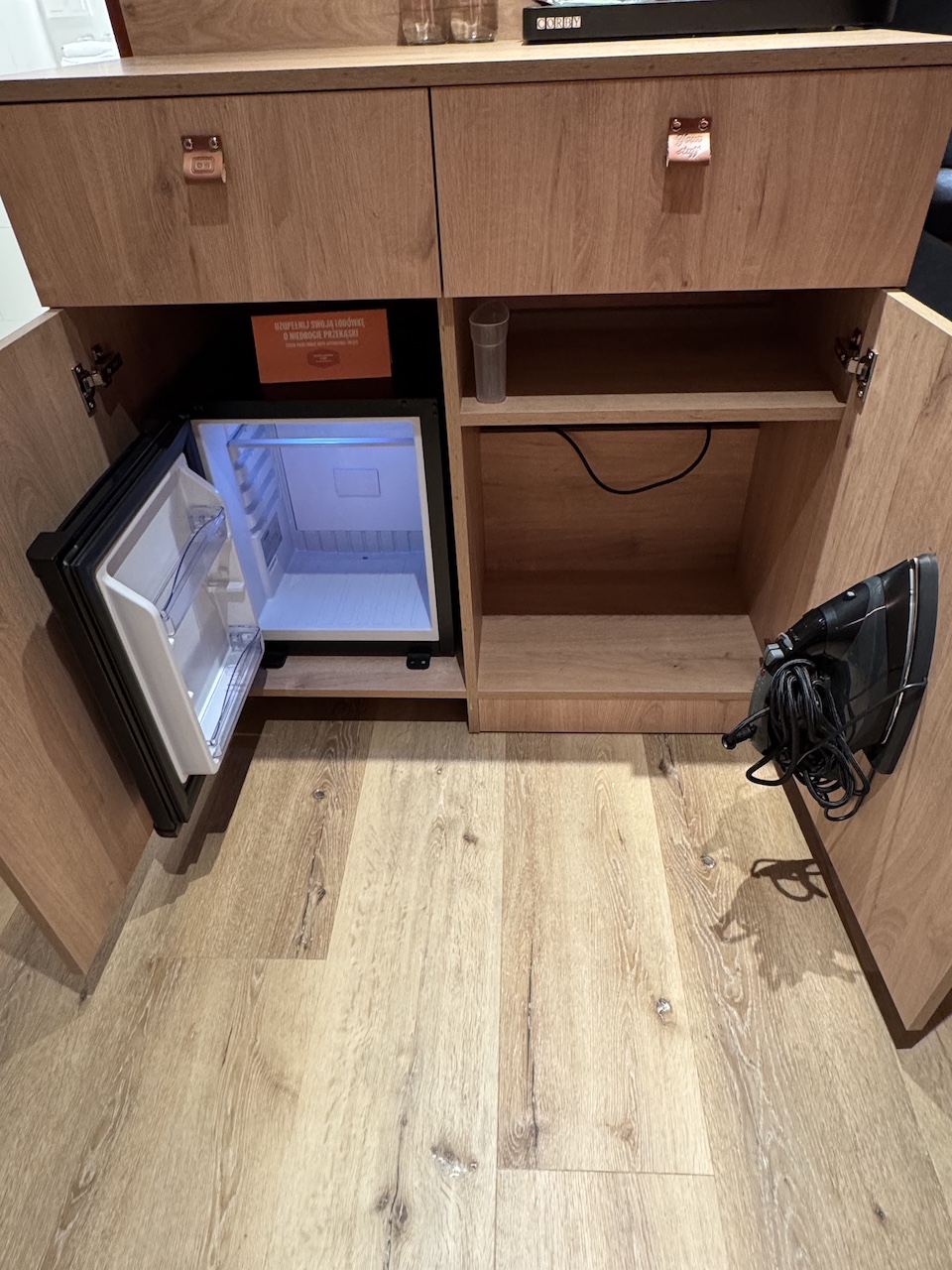 Geöffneter Holzunterschrank mit leerem Mini-Kühlschrank links und Haartrockner rechts.