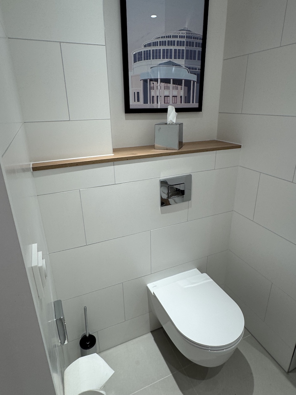 Modernes Gäste-WC mit wandhängendem WC, weißen Großformatfliesen, Holzablage und Architekturfoto.