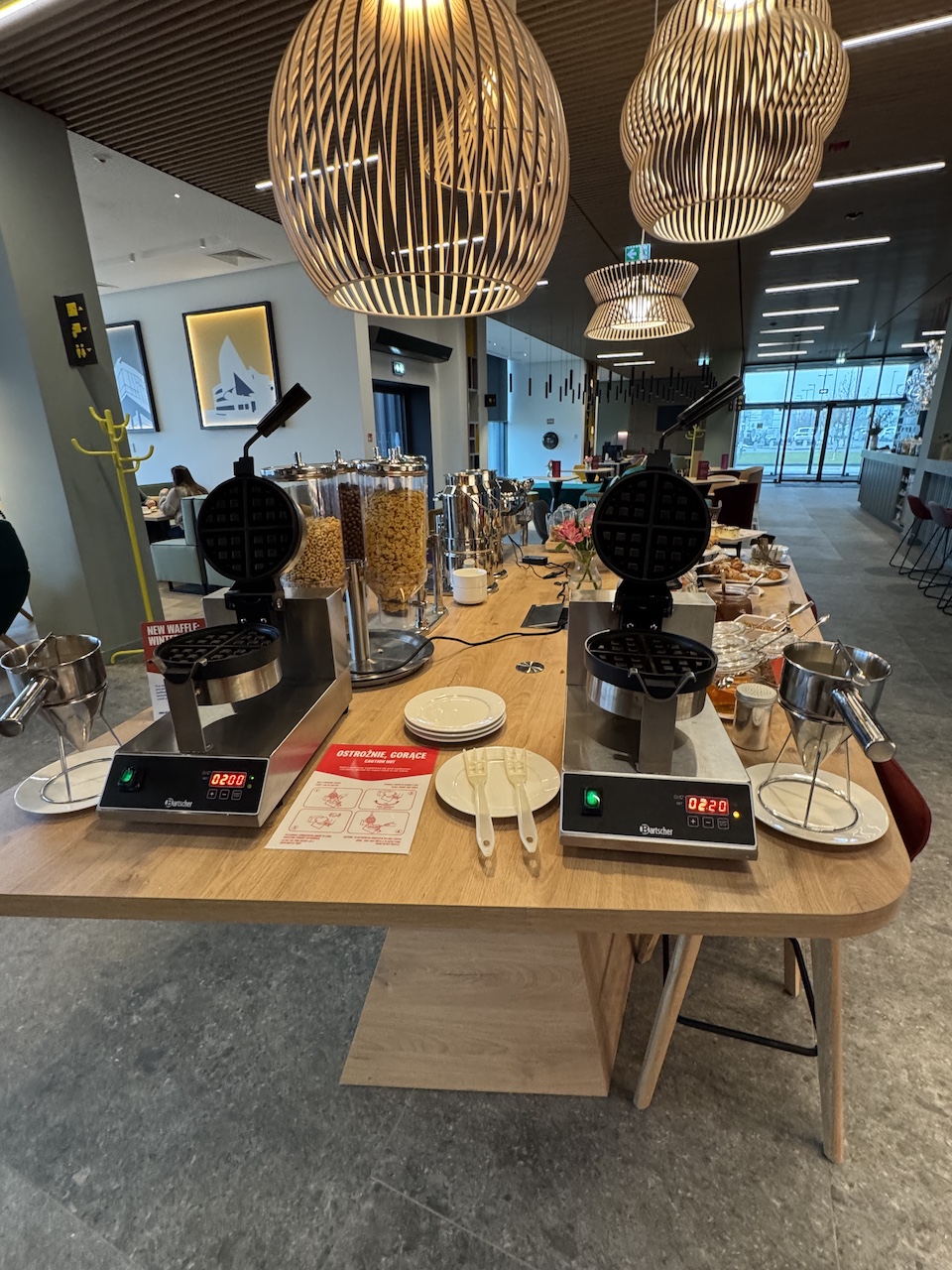 Zwei Waffeleisen der Marke Bartscher auf einem Holztisch, daneben Cerealienspender, Teller und Beilagen.