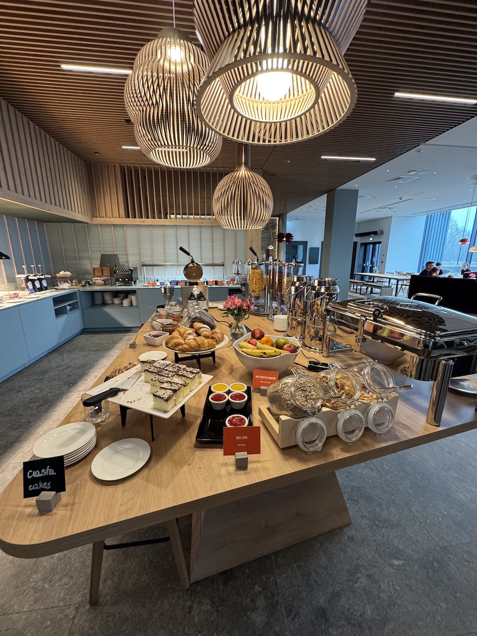 Frühstücksbuffet mit Croissants, Obst, Müsli, Aufschnitt und Chafing Dishes auf einem Holztisch.