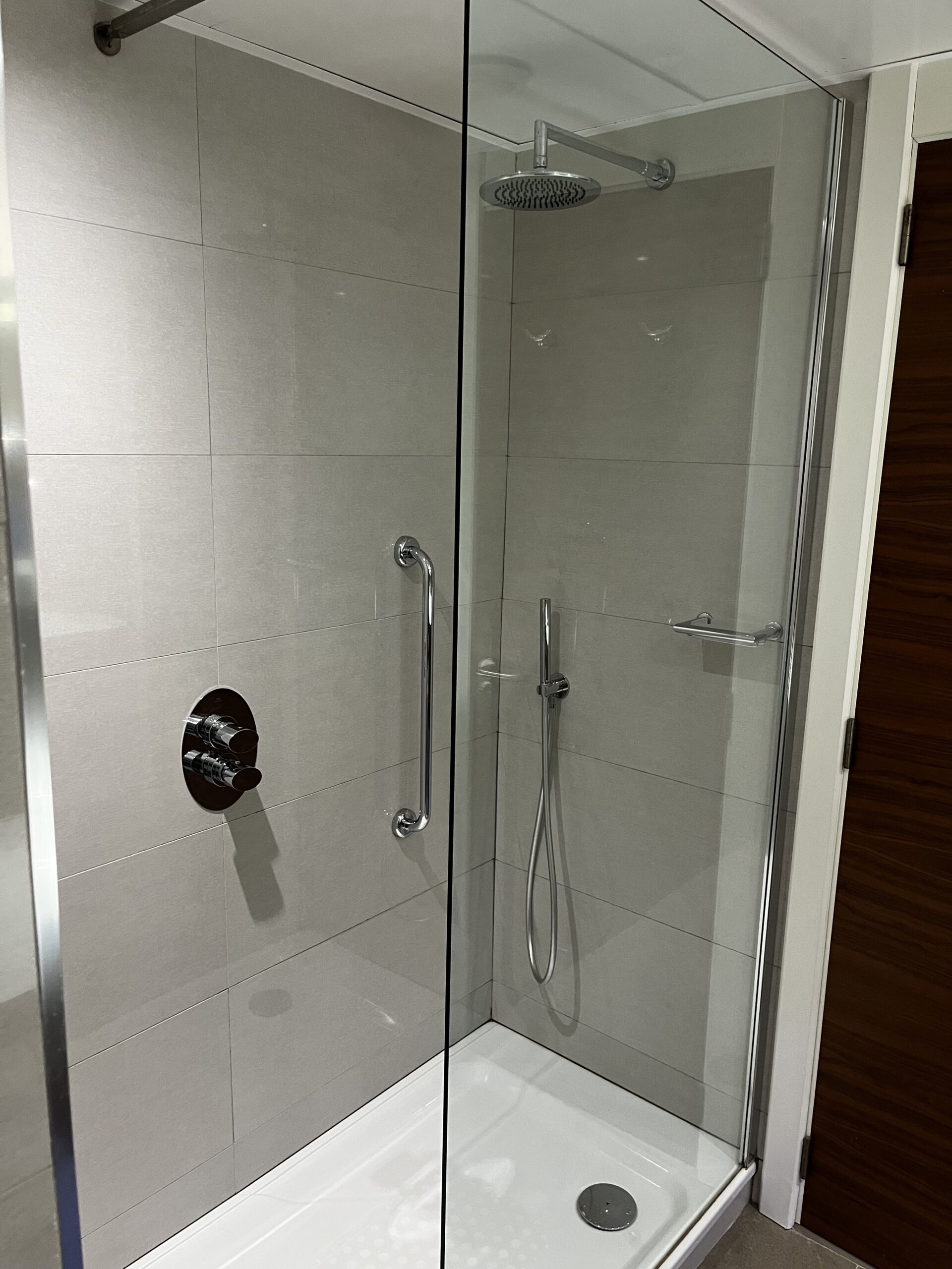 Duschkabine mit Glastür, Regendusche, Handbrause und rundem Thermostatmischer an grauer Fliesenwand.