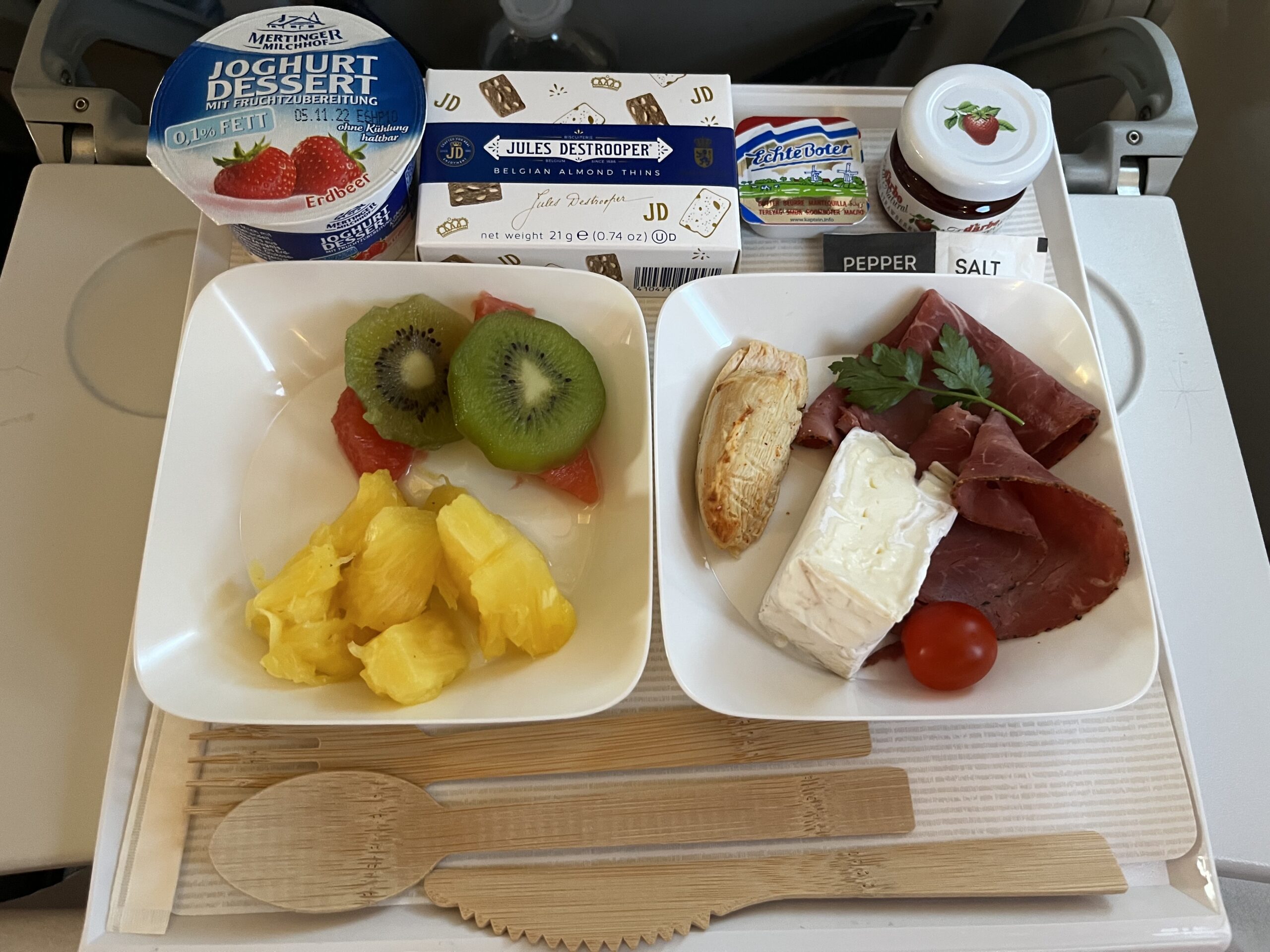 Tablett mit zwei Tellern: Obstsalat mit Kiwi und Ananas, Aufschnitt mit Brie und Tomate. Dazu Erdbeerjoghurt, Butter, Kekse.