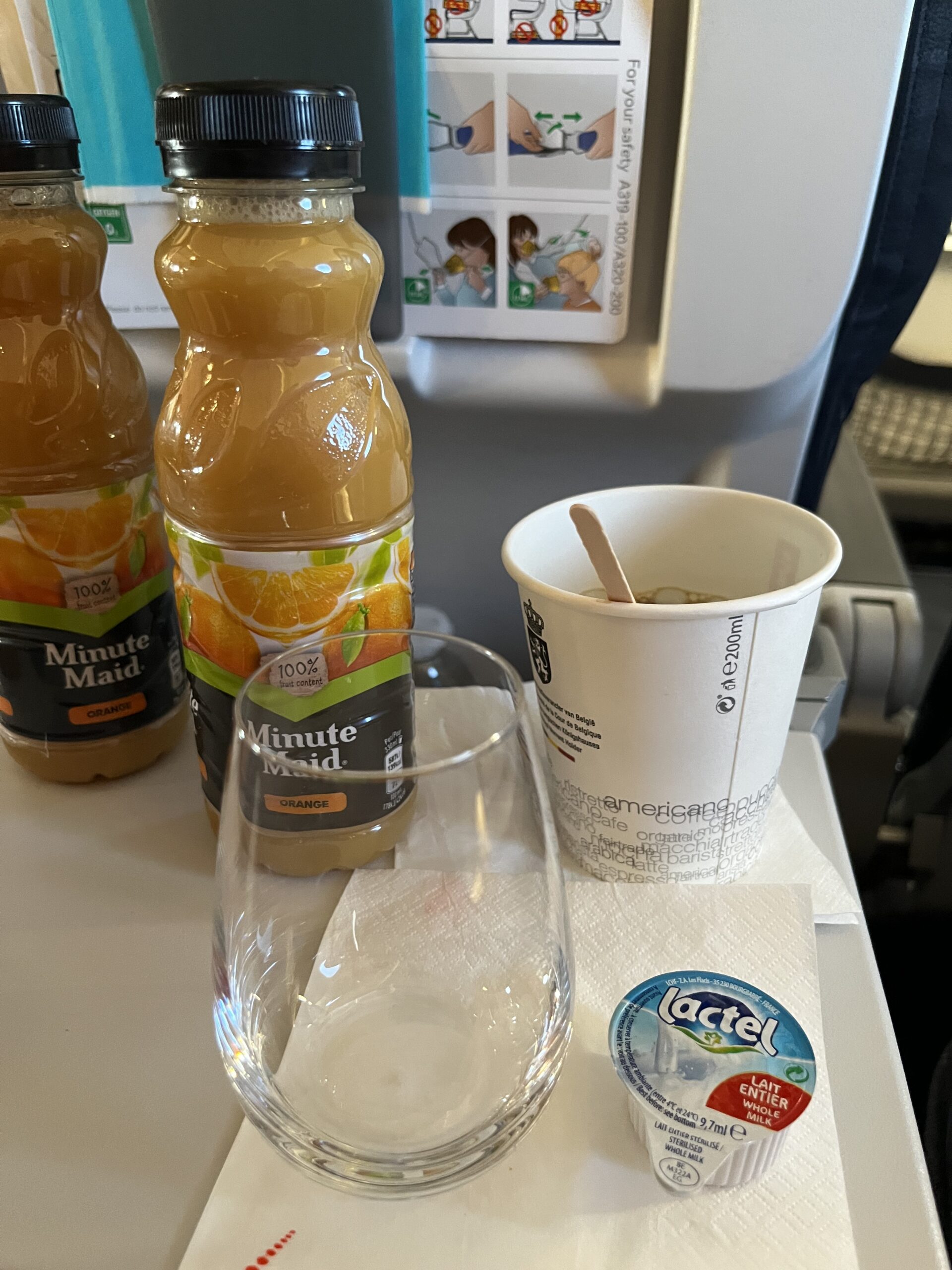 Zwei Minute-Maid-Orangensaftflaschen, ein leeres Glas, ein Pappbecher mit Rührstäbchen und ein Lactel-Milchportionsbehälter a
