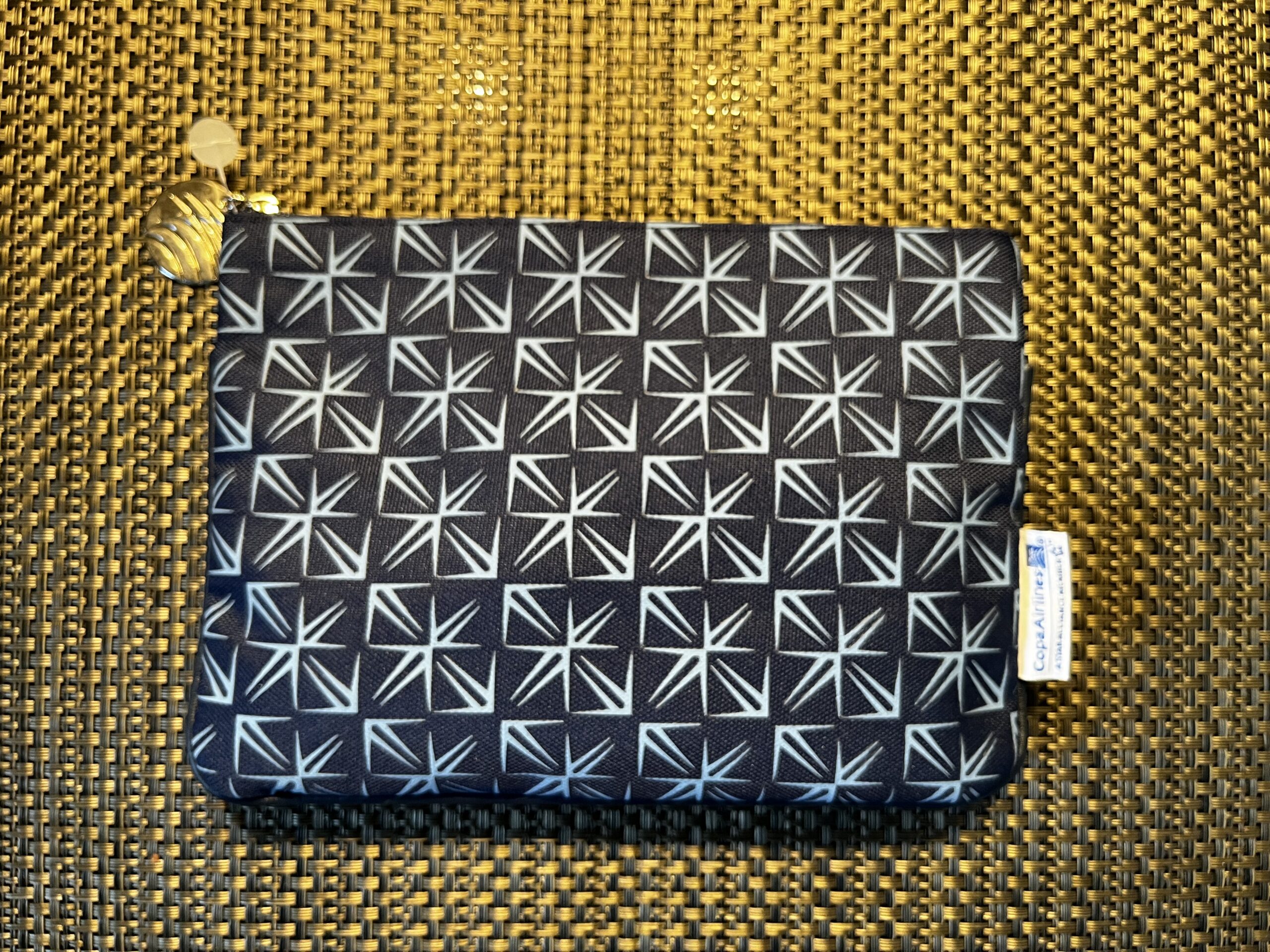 Schwarzes Amenity-Kit von Copa Airlines mit weißem geometrischem Muster und goldenem Reißverschluss-Zipper.