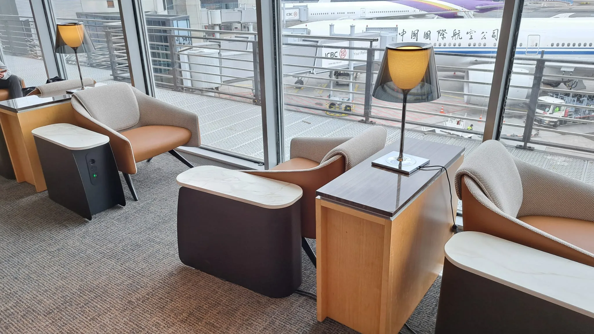 Lounge mit Sesseln und Tischen vor Flughafenfenster