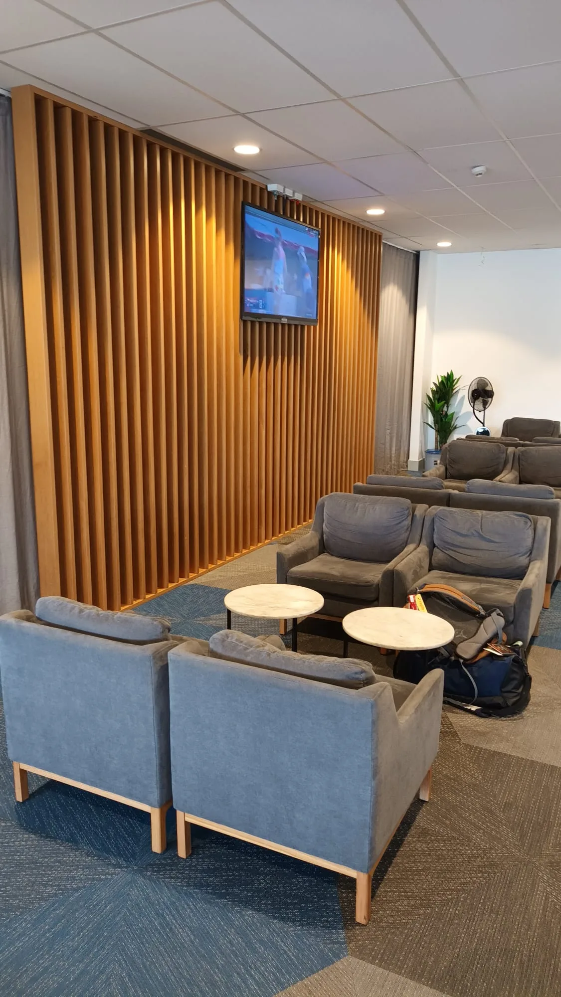 Lounge mit Sesseln und Tischen vor Holzwand