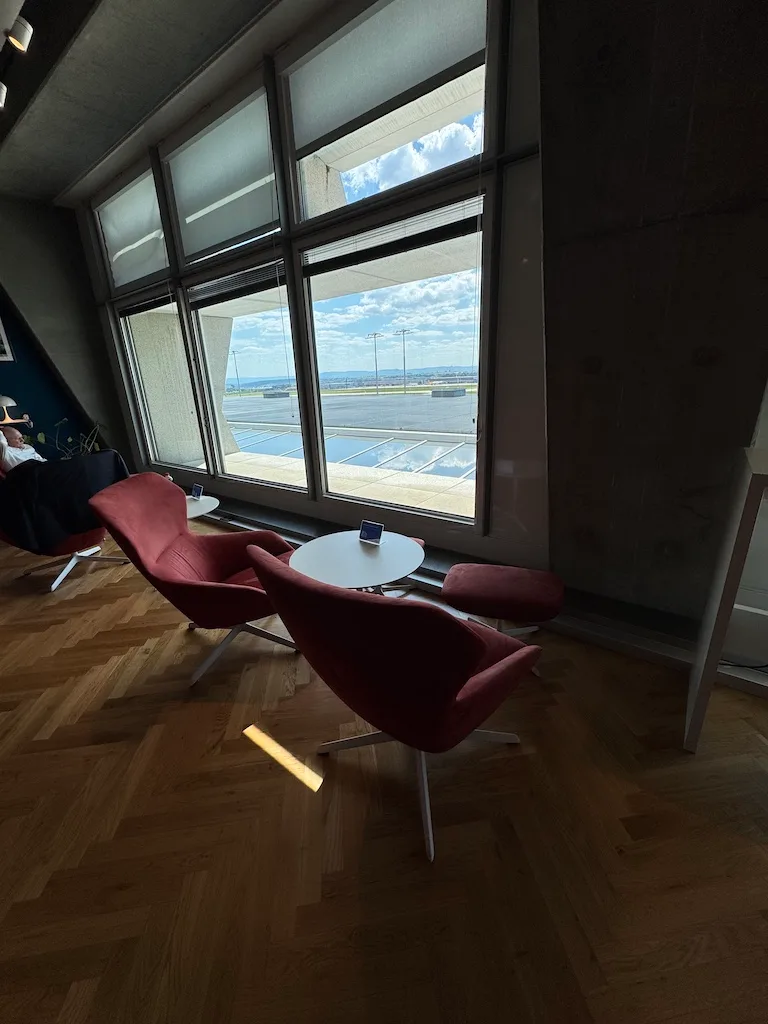 Lounge mit roten Sesseln und Tisch vor Fenster mit Flugfeldblick