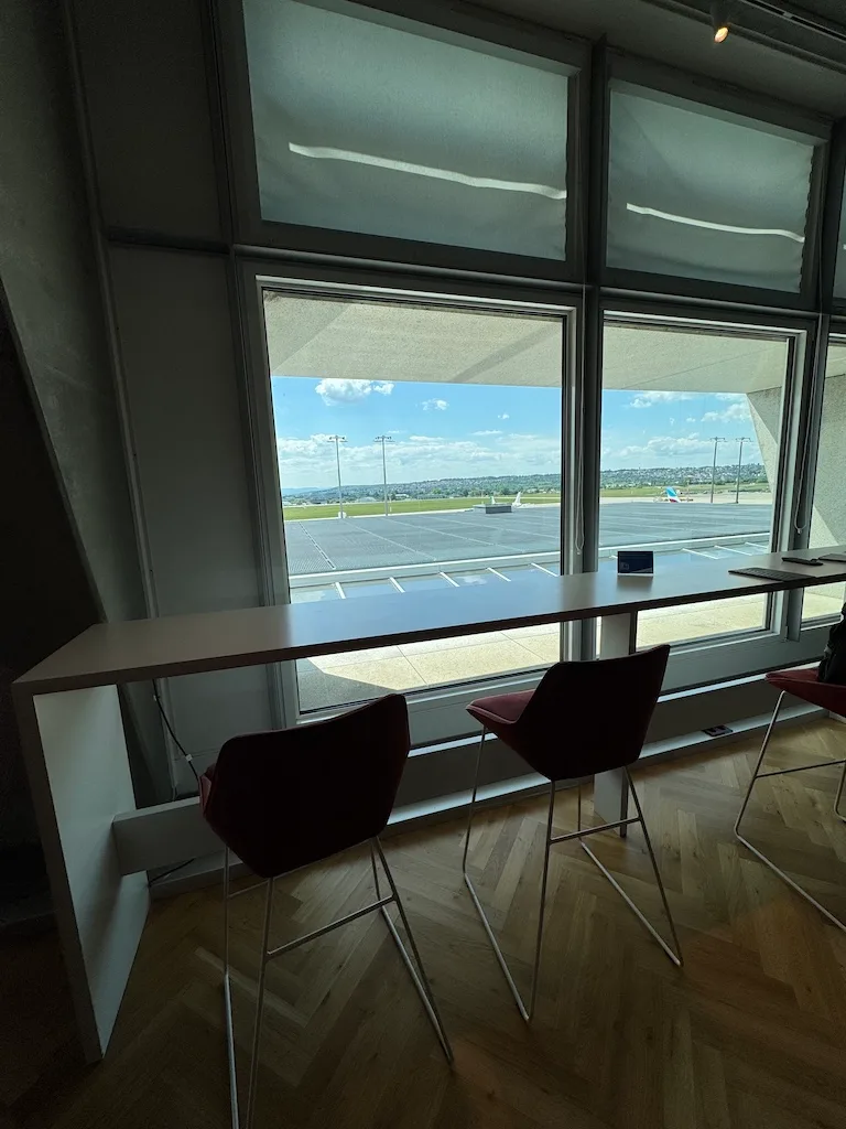Lounge mit Tischen und Stühlen vor Fenster mit Flughafenaussicht