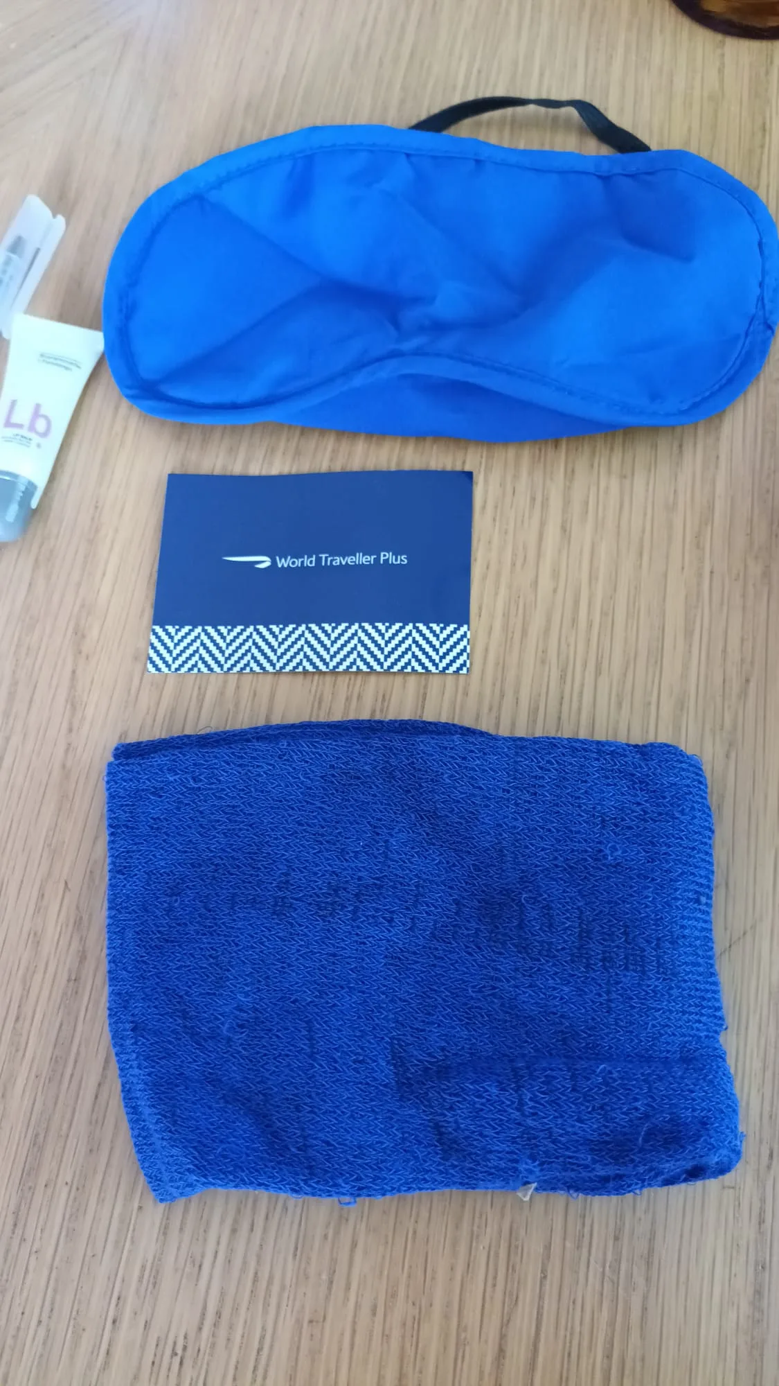 Blauer Schlafmaske, Handtuch und Karte mit 'World Traveller Plus' auf Holztisch
