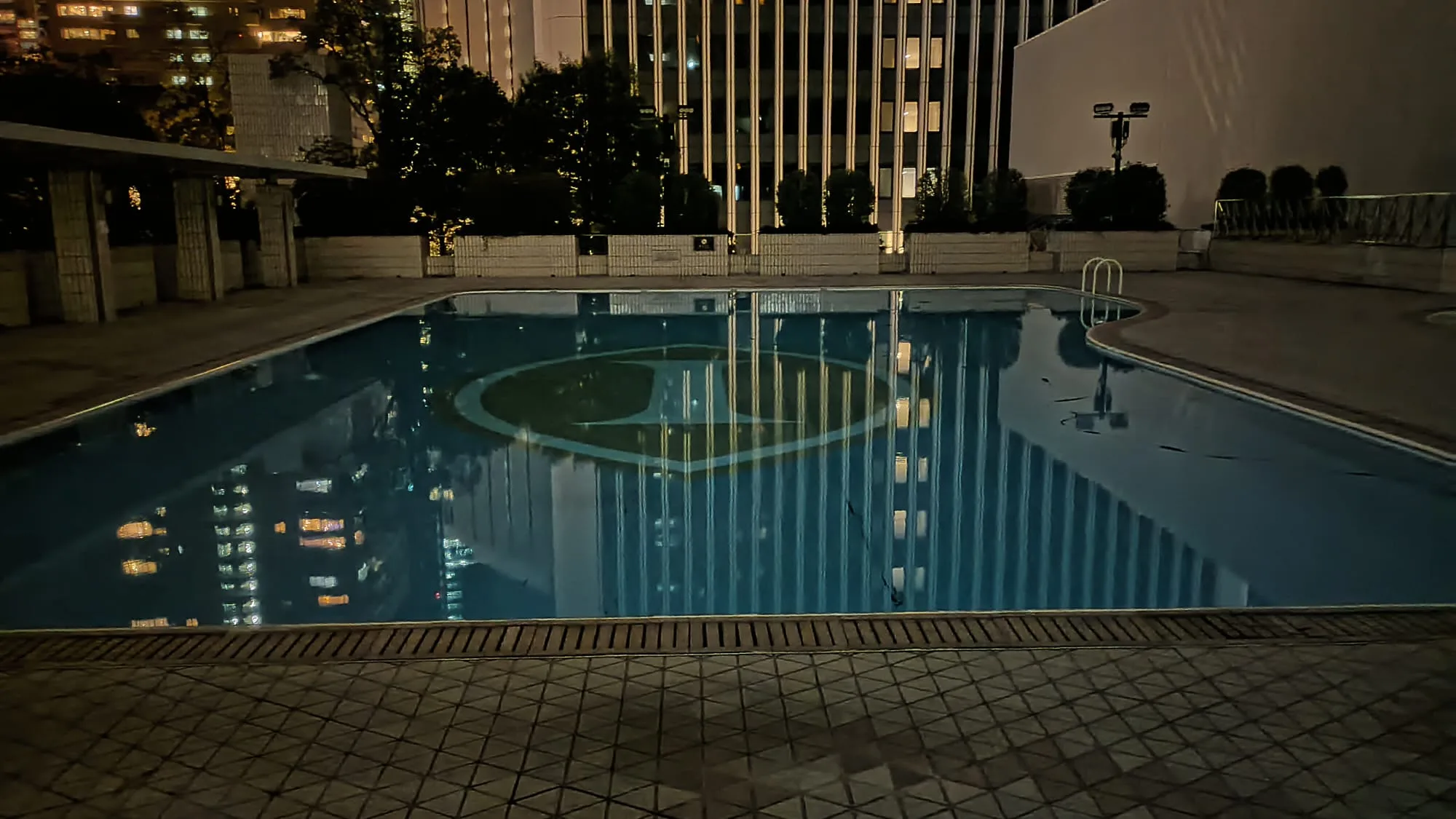 Nachtansicht eines Poolbereichs mit reflektierendem Wasser und umgebenden Gebäuden