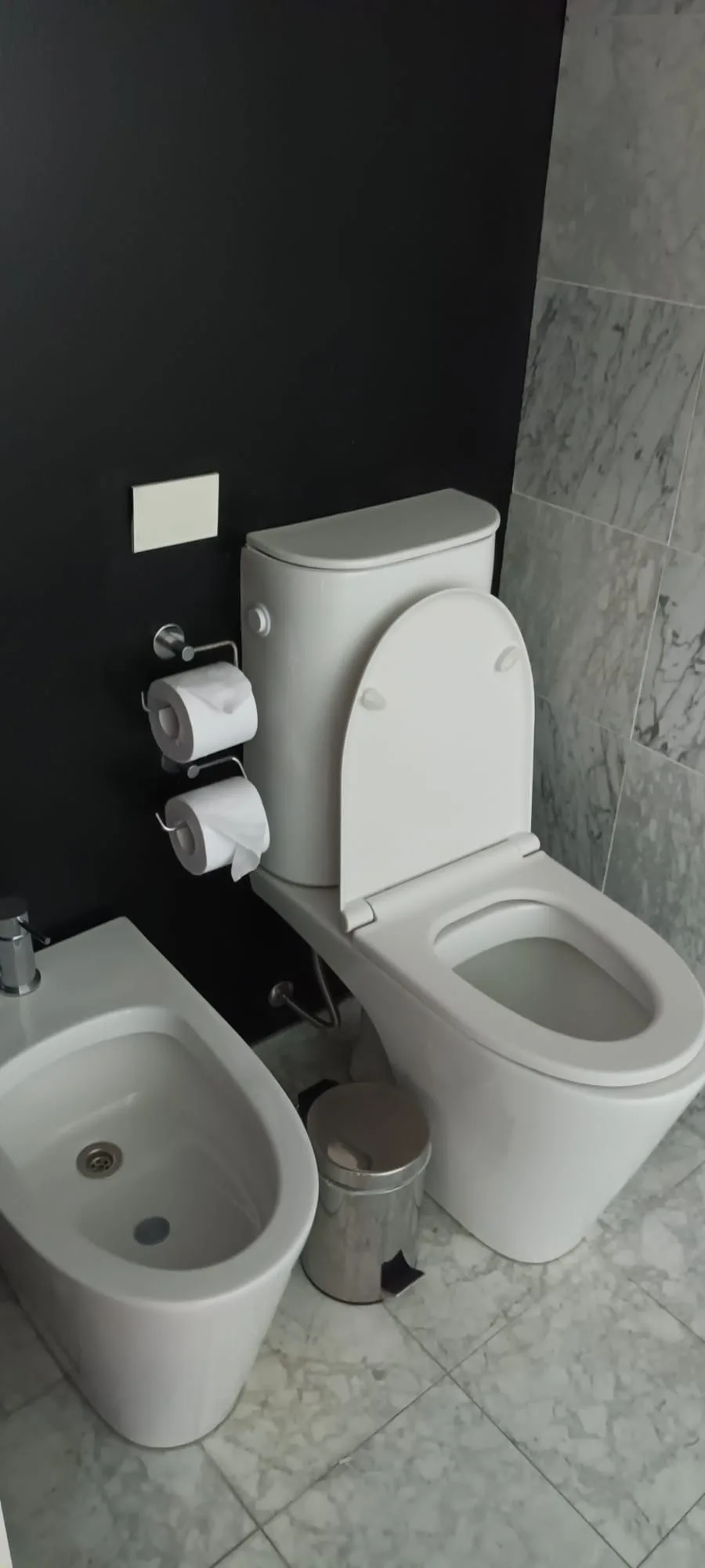 Moderne Toilette mit Bidet und Papierrollenhalter an der Wand