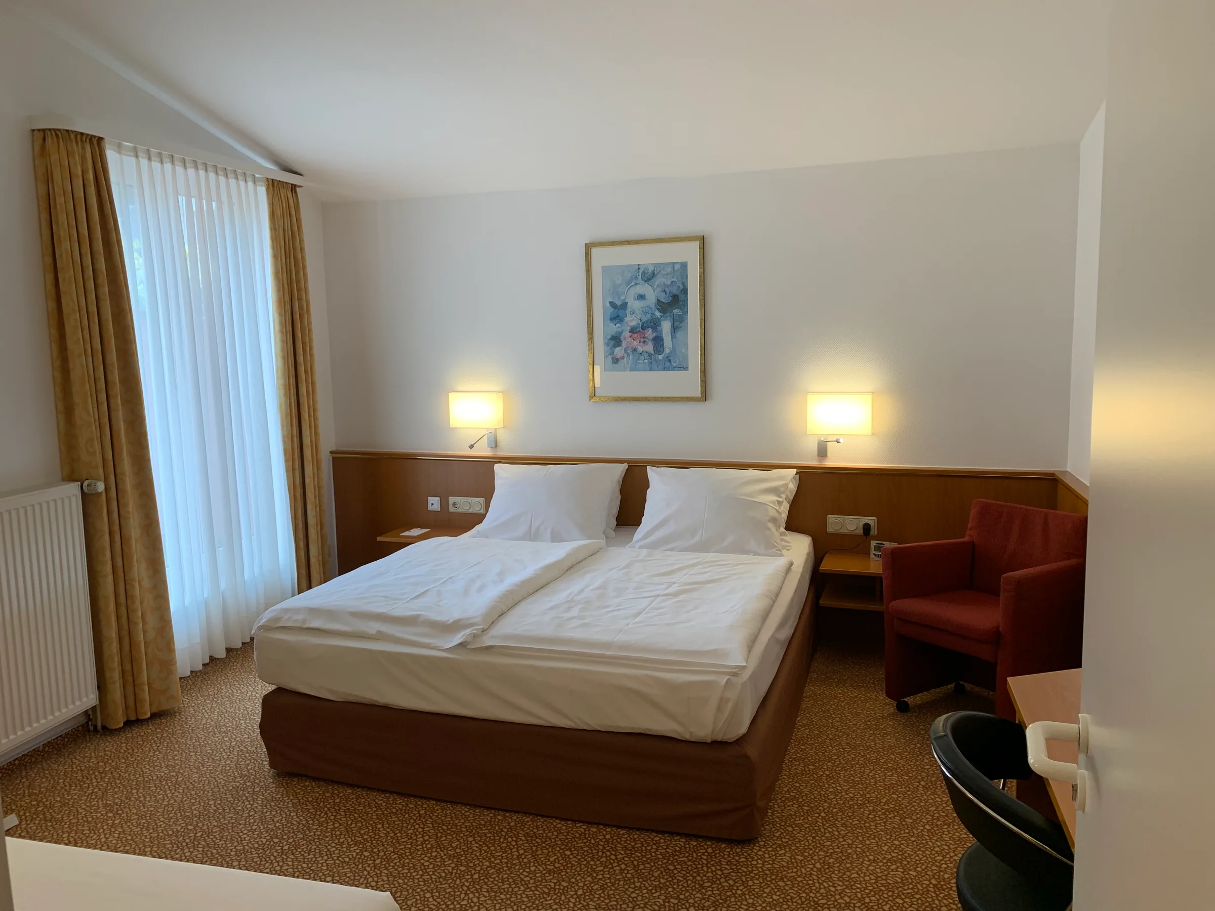 Hotelzimmer mit Doppelbett und Sessel in warmen Farbtönen