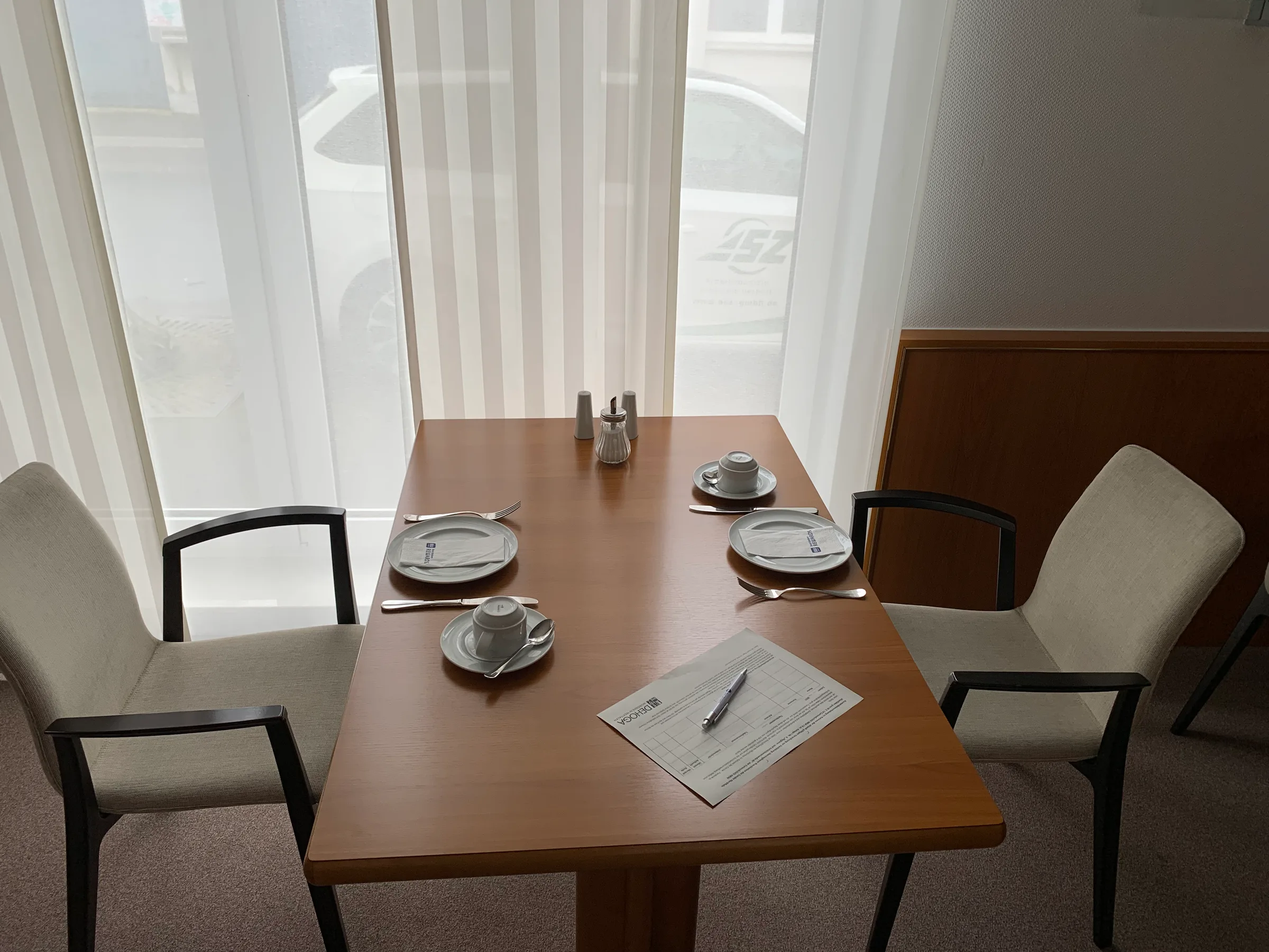 Hotelzimmer mit Tisch und Stühlen vor Fenster mit Vorhängen