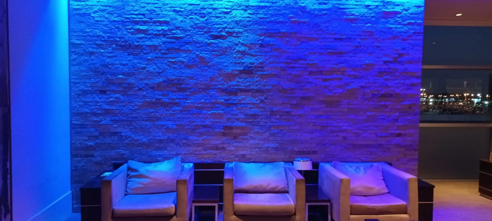 Lounge mit blau beleuchteter Steinwand und weißen Sesseln