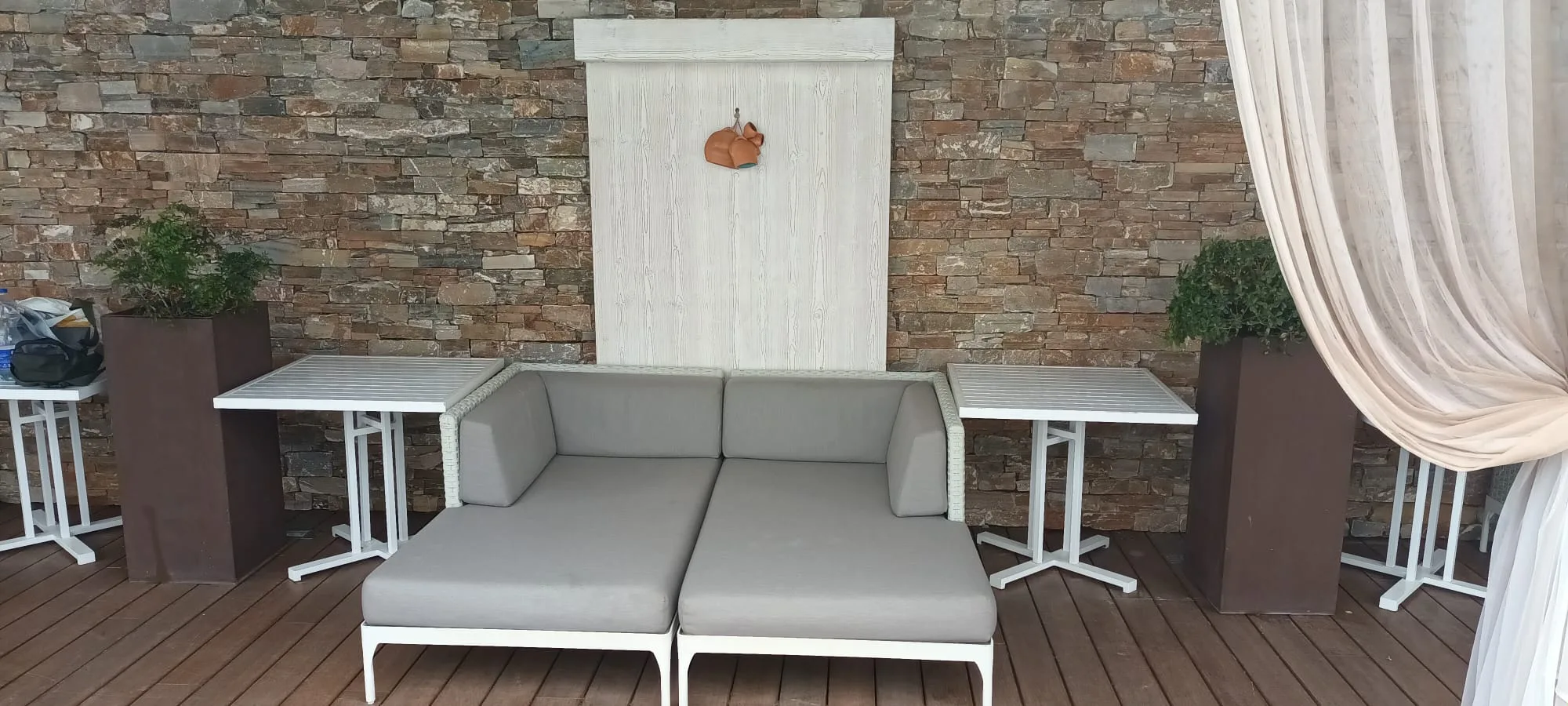 Terrasse mit Sofa und Tischen vor Steinwand