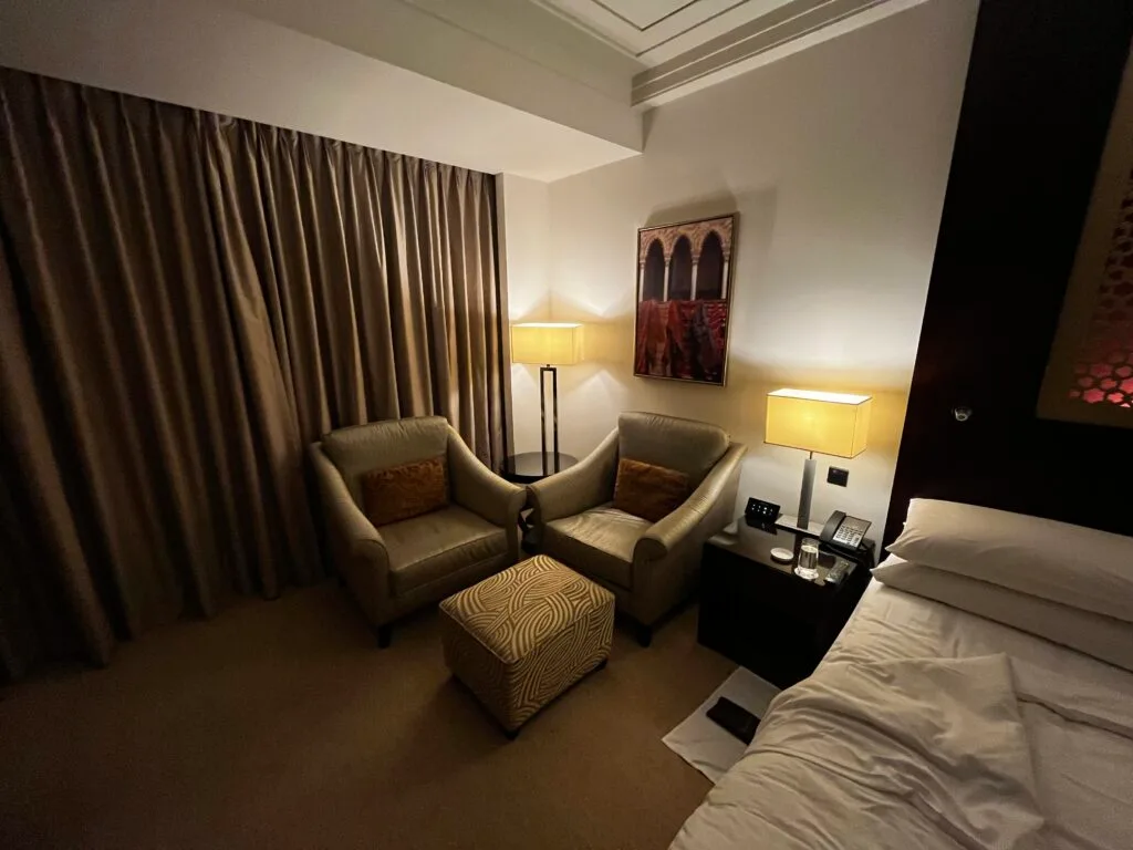 Hotelzimmer mit Doppelbett und Sessel in warmen Farbtönen