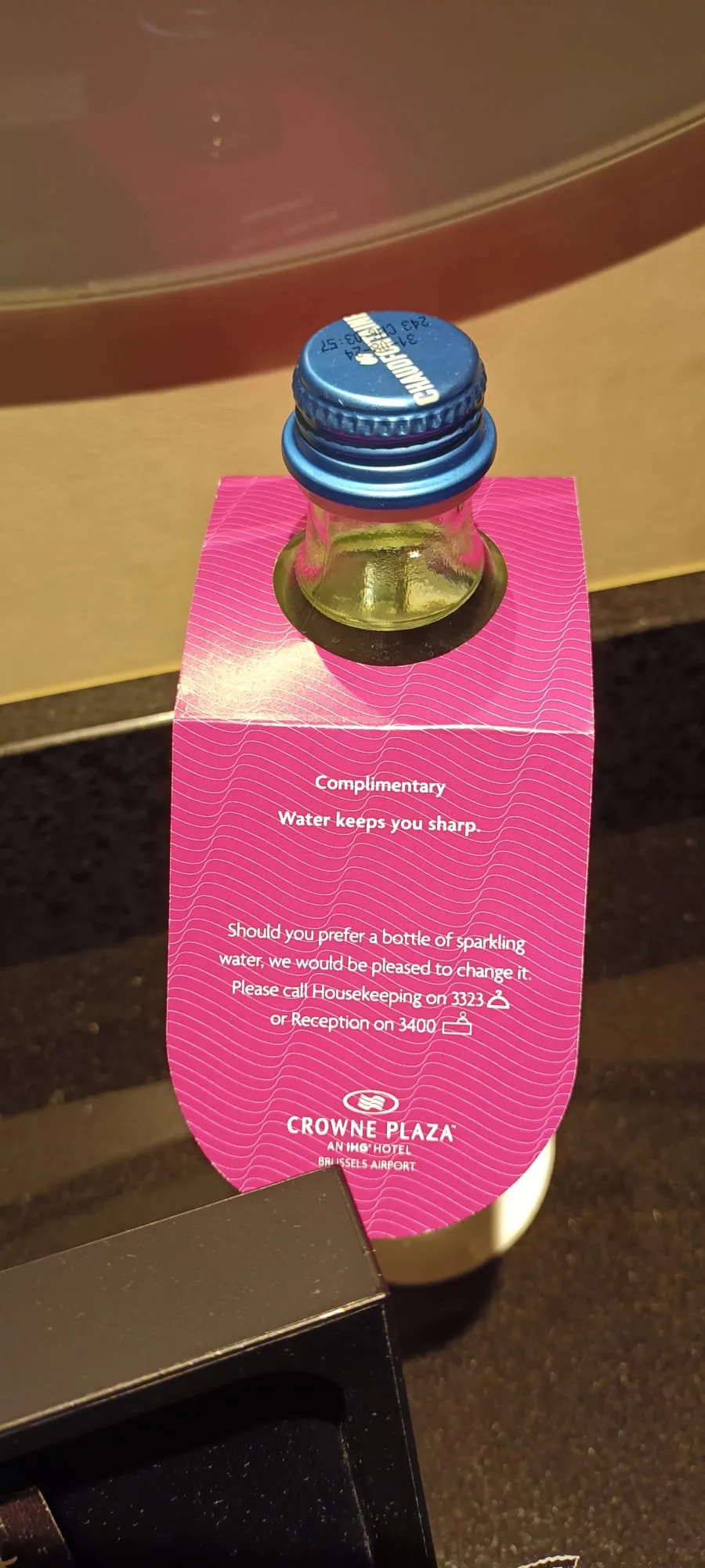Gästewasserflasche mit rosa Etikett und Text auf dem Hotelzimmer