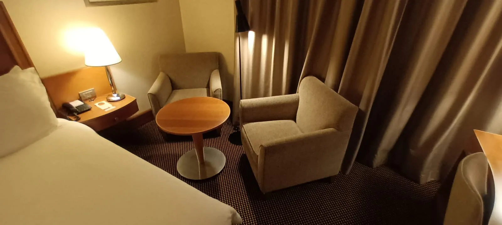Hotelzimmer mit Doppelbett, Nachttisch und Sessel in neutralen Farben