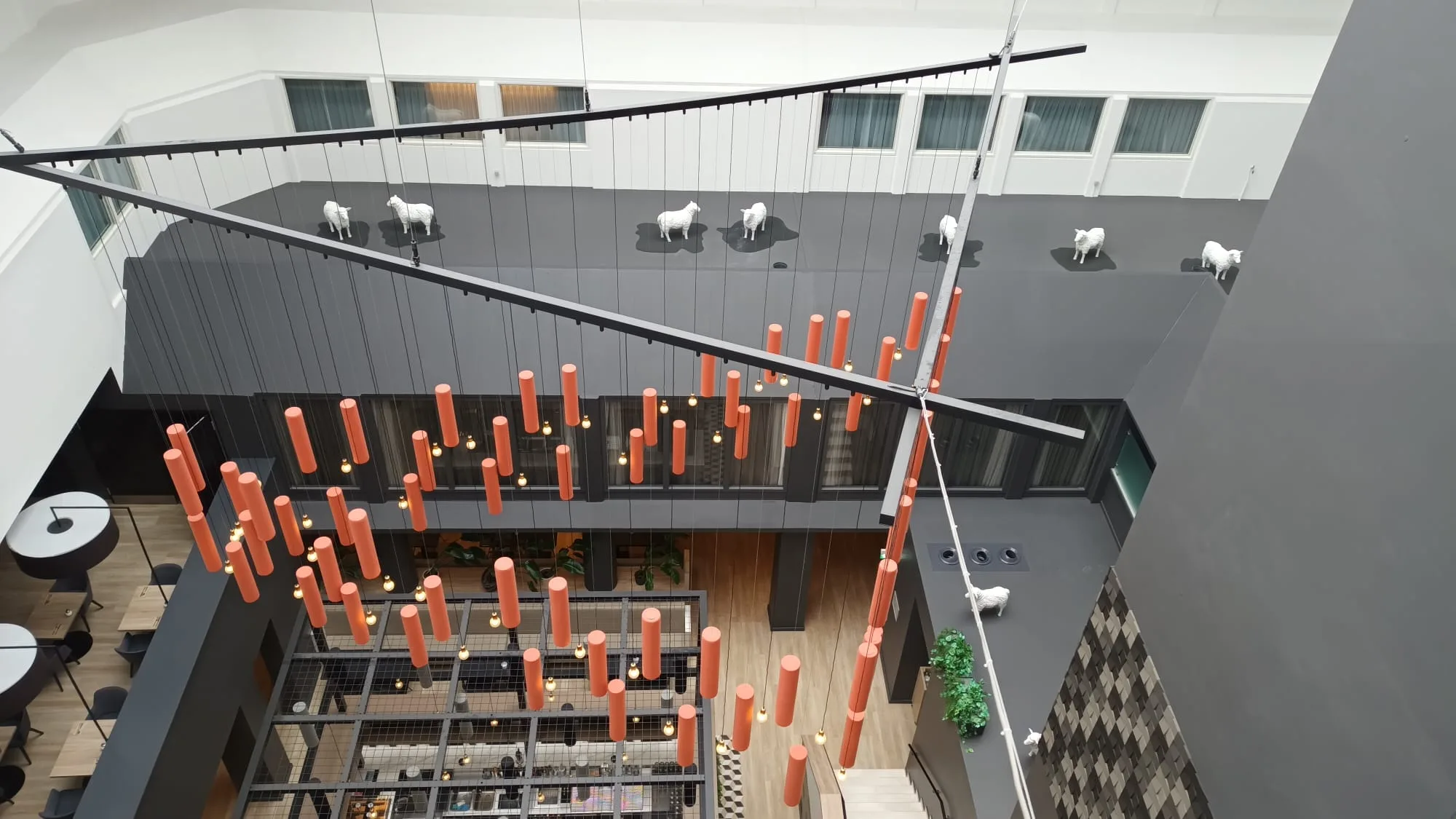 Hochflur-Hotellobby mit schwebenden Schafen und orangefarbenen Pendelleuchten