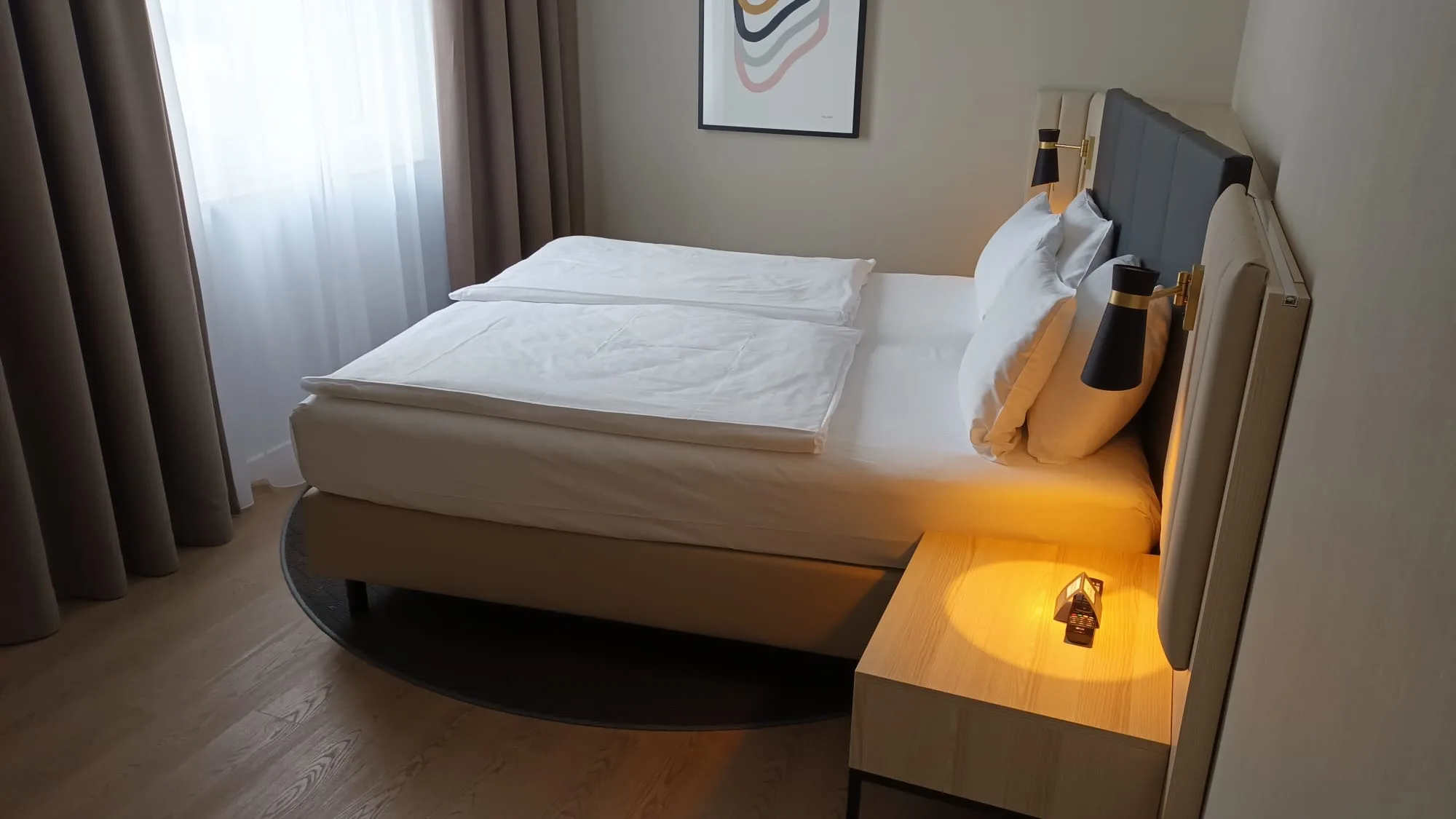 Doppelbett im Hotelzimmer mit grauen Vorhängen und Nachttischlampe