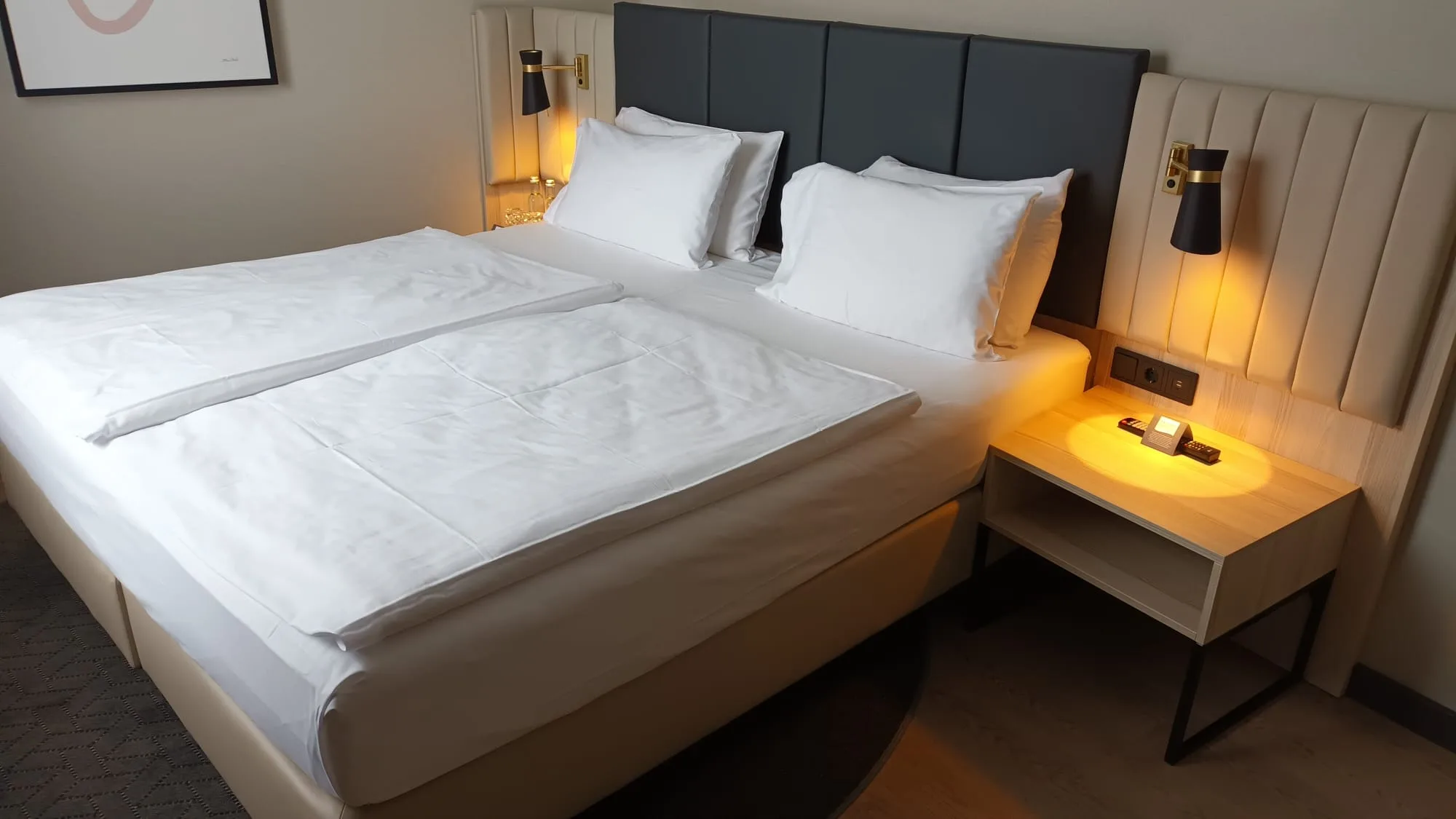 Doppelbett im Hotelzimmer mit grauem Kopfteil und Nachttisch