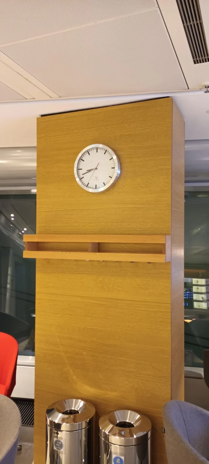 Holzpaneel mit Uhr und Müllbehältern im Flughafensalon