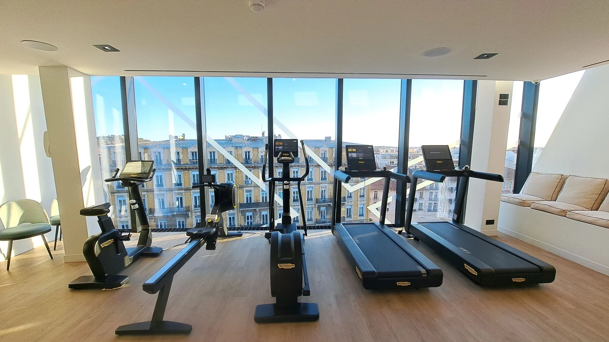 Fitnessraum mit Laufbändern und Fahrrädern vor großem Fenster