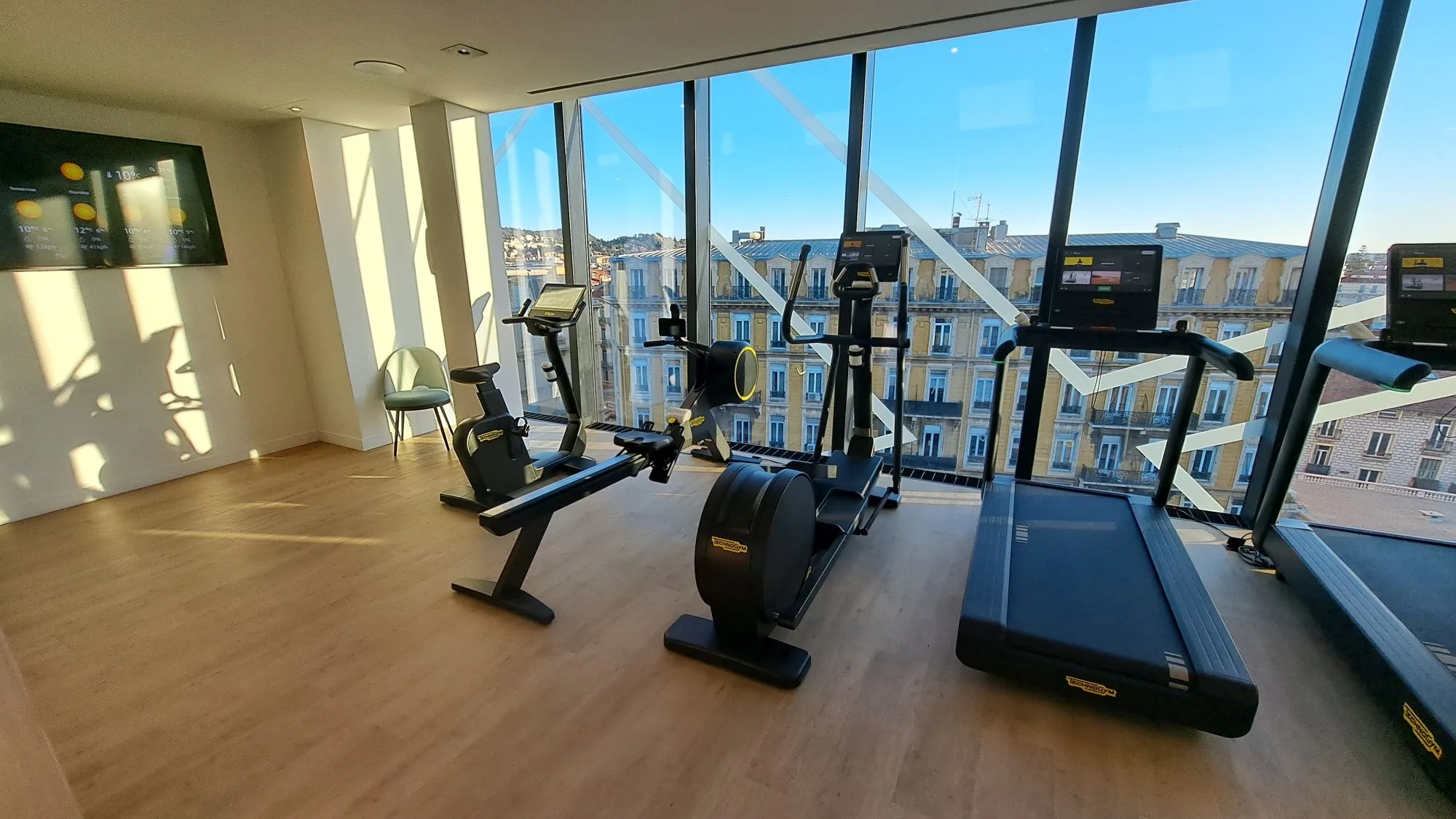 Fitnessraum mit Laufband, Fahrrad und Elliptical Trainer vor großem Fenster