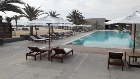 Poolbereich mit Liegestühlen und Sonnenschirmen am Strand