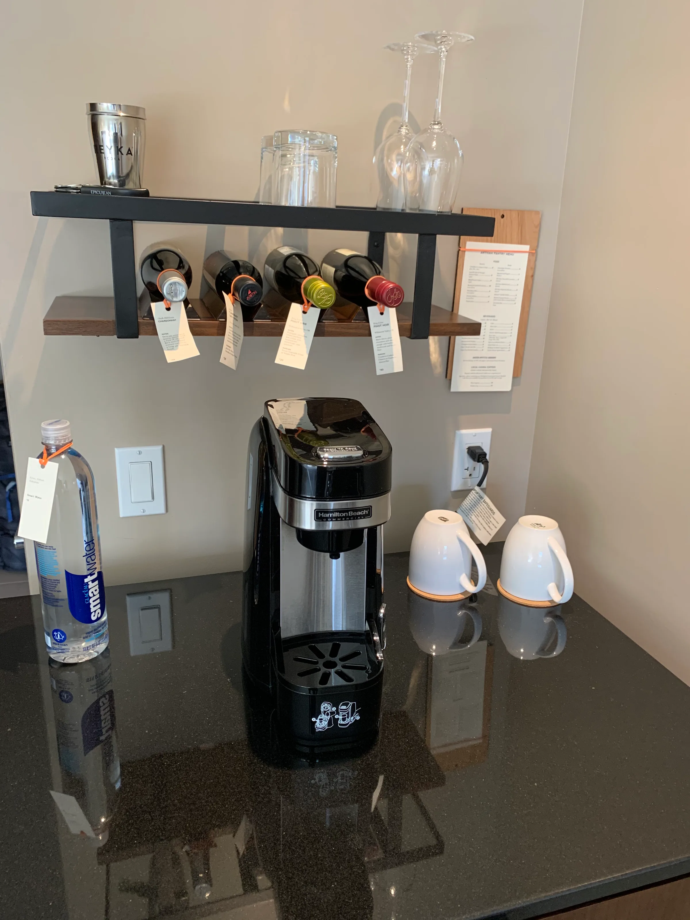 Hotelzimmerecke mit Kaffeemaschine, Flasche und Regal mit Gläsern und Weinflaschen