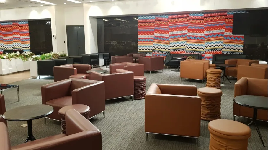 Lounge mit orangefarbenen Sesseln und buntem Wandteppich