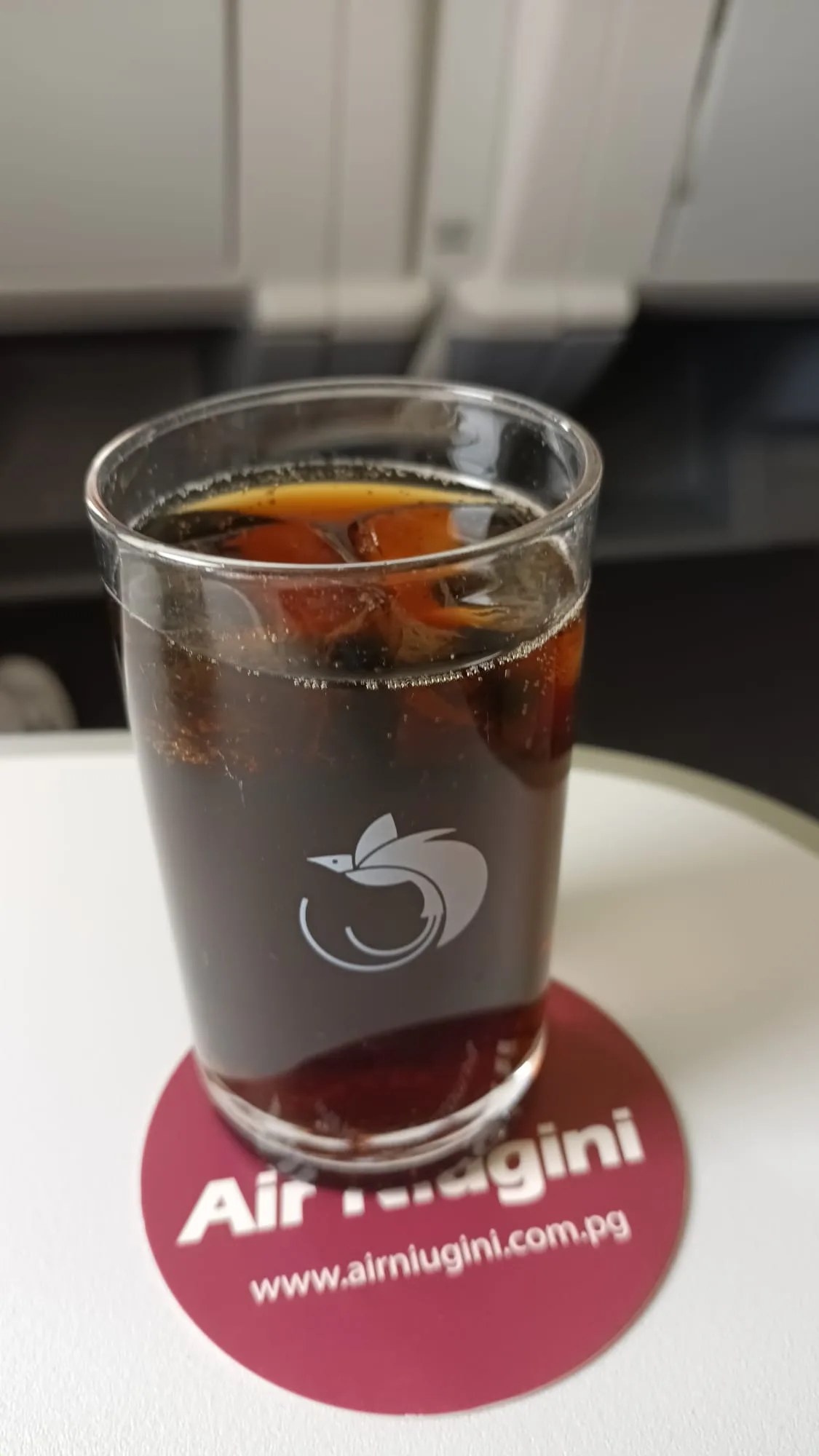 Glas mit Eiswürfeln und dunklem Getränk auf Untersetzer mit Air Niugini-Logo