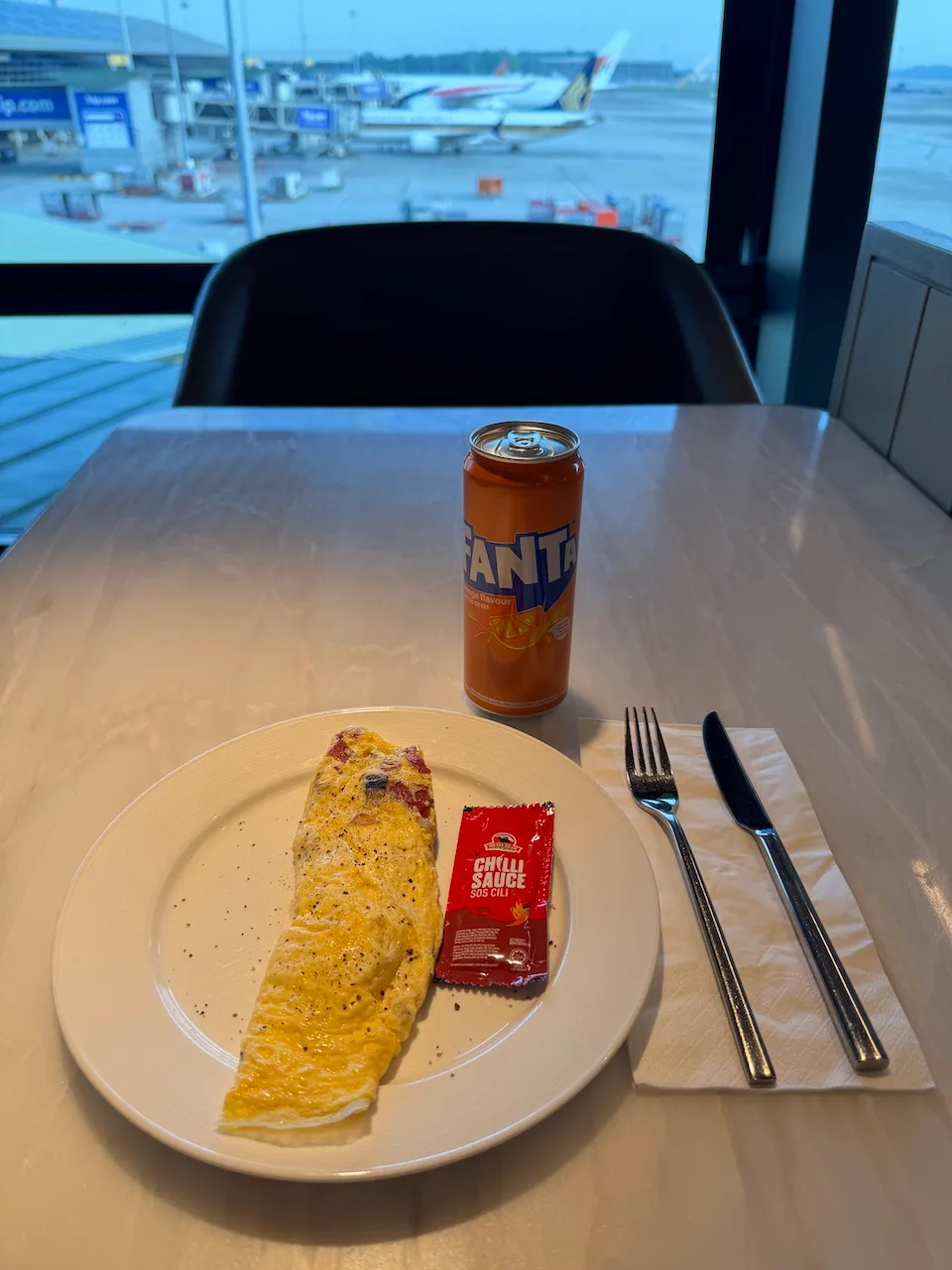 Omelett auf Teller mit Flasche Fanta und Chili-Sauce-Packung