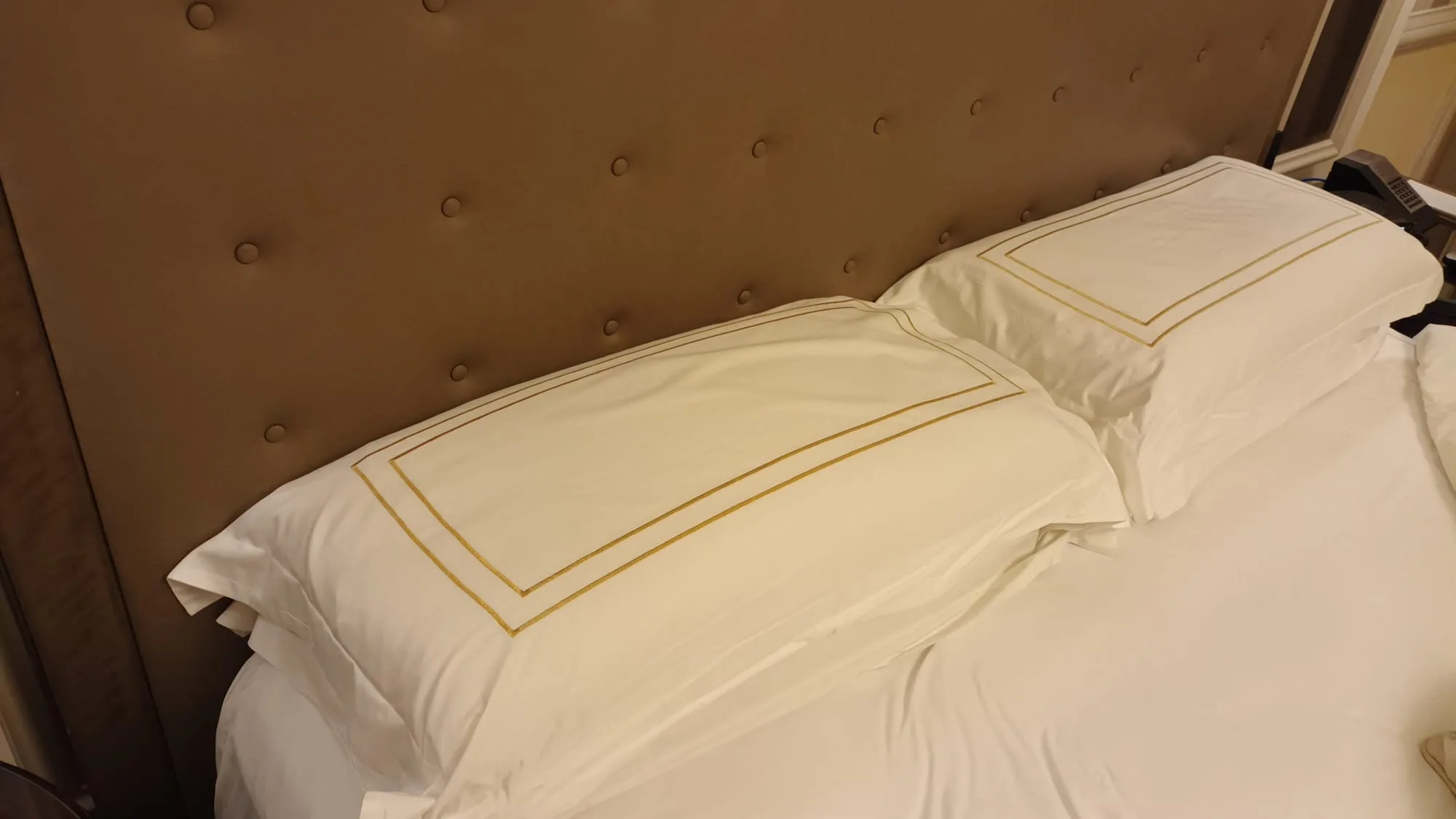 Doppelbett mit weißen Kissen und goldener Stickerei im Hotelzimmer