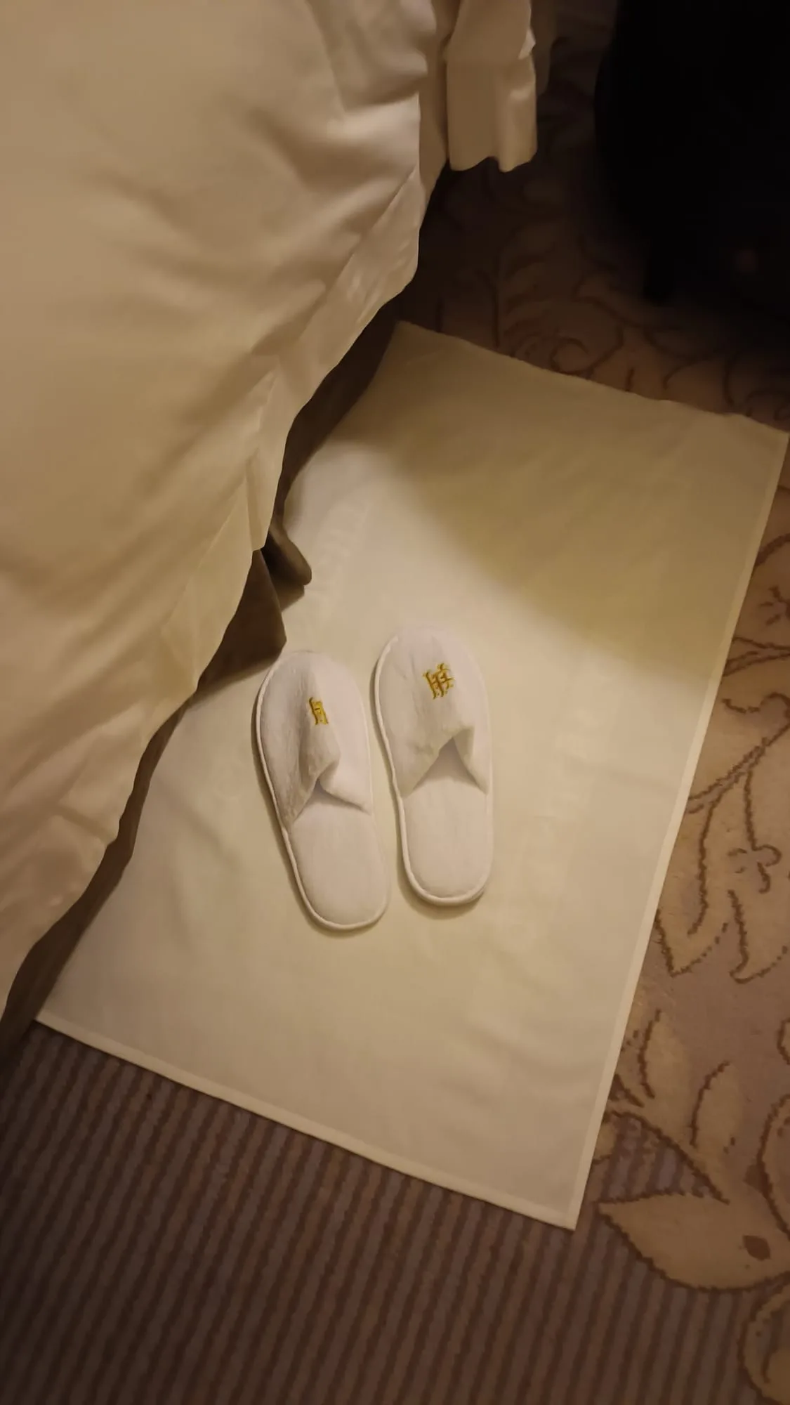 Weißer Slippers auf Handtuch vor Bett