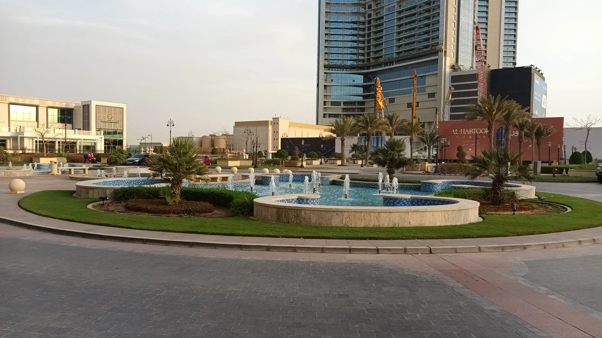 Garten mit Brunnen und Palmen vor modernem Gebäudekomplex