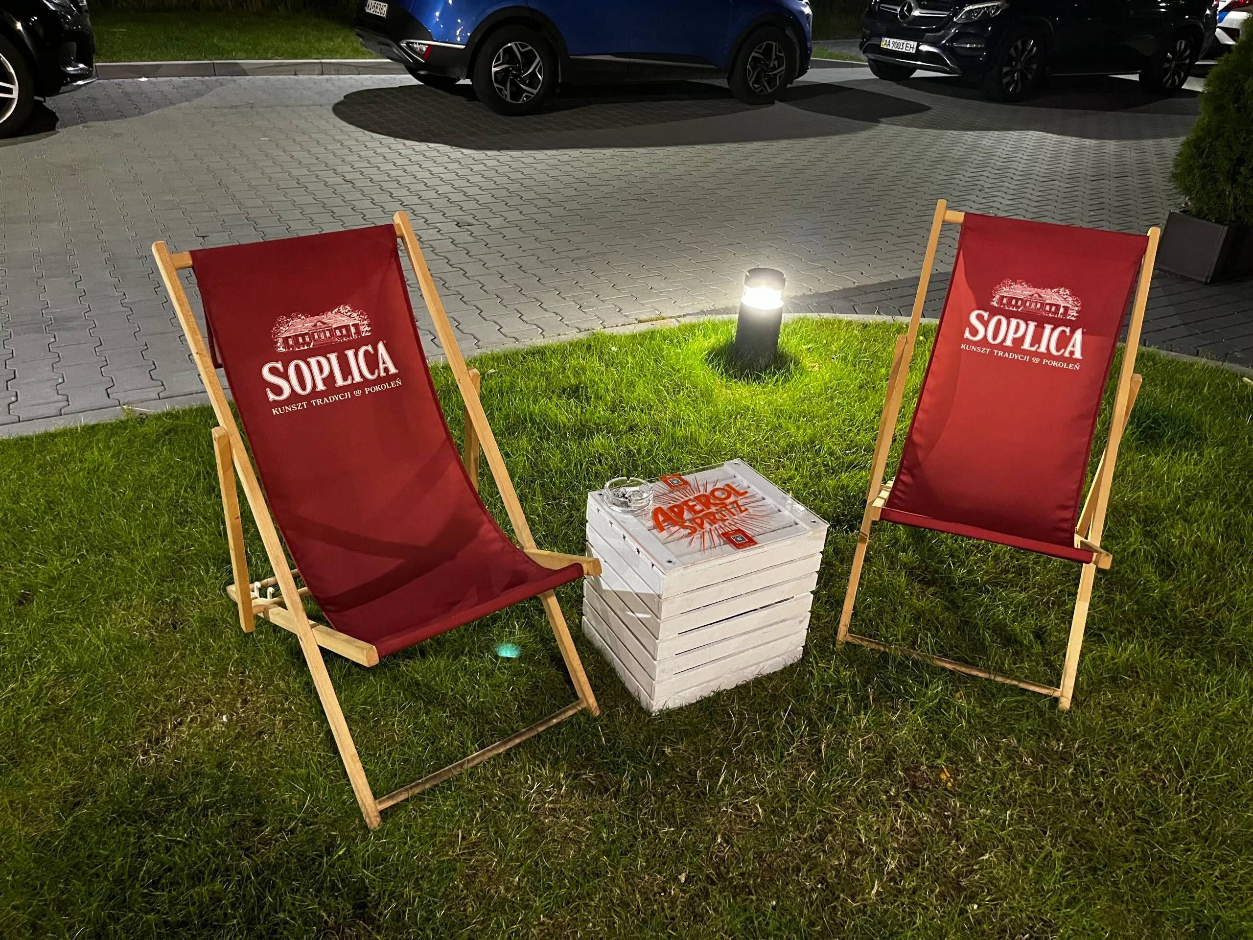 Zwei Liegestühle mit Soplica-Logo auf Gras vor Parkplatz