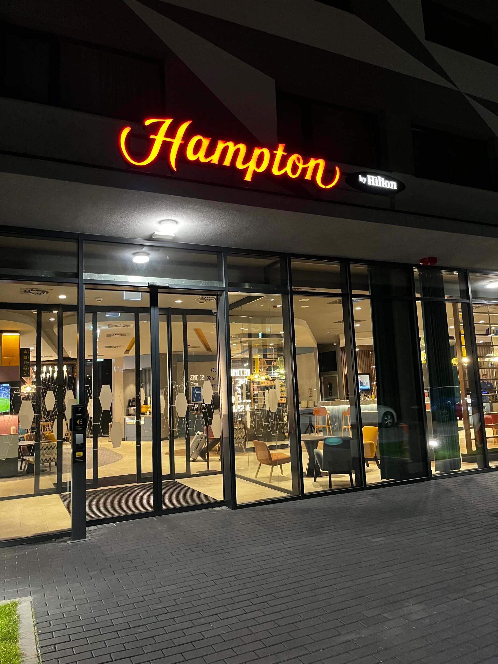 Hotel Eingang mit Neon-Schild 'Hampton by Hilton' bei Nacht
