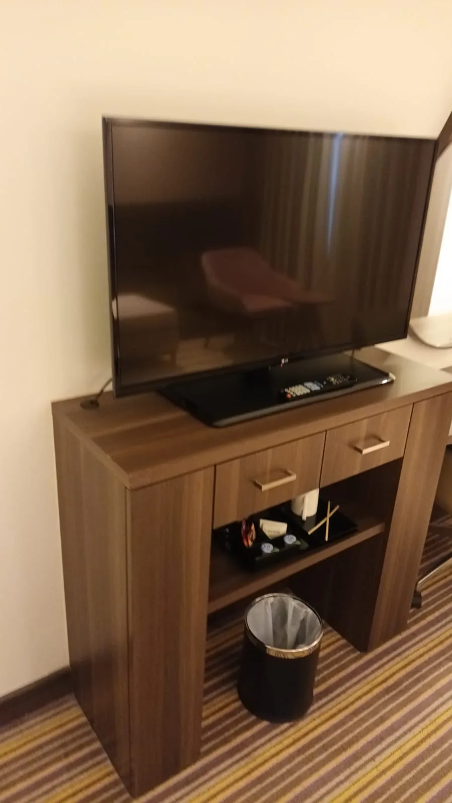 Hotel-TV auf Holzregal mit Fernbedienung und Papierkorb darunter