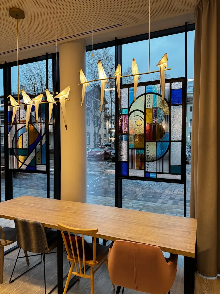 Hotellobby mit Holztisch und Stühlen, Fenster mit abstraktem Glasmosaik