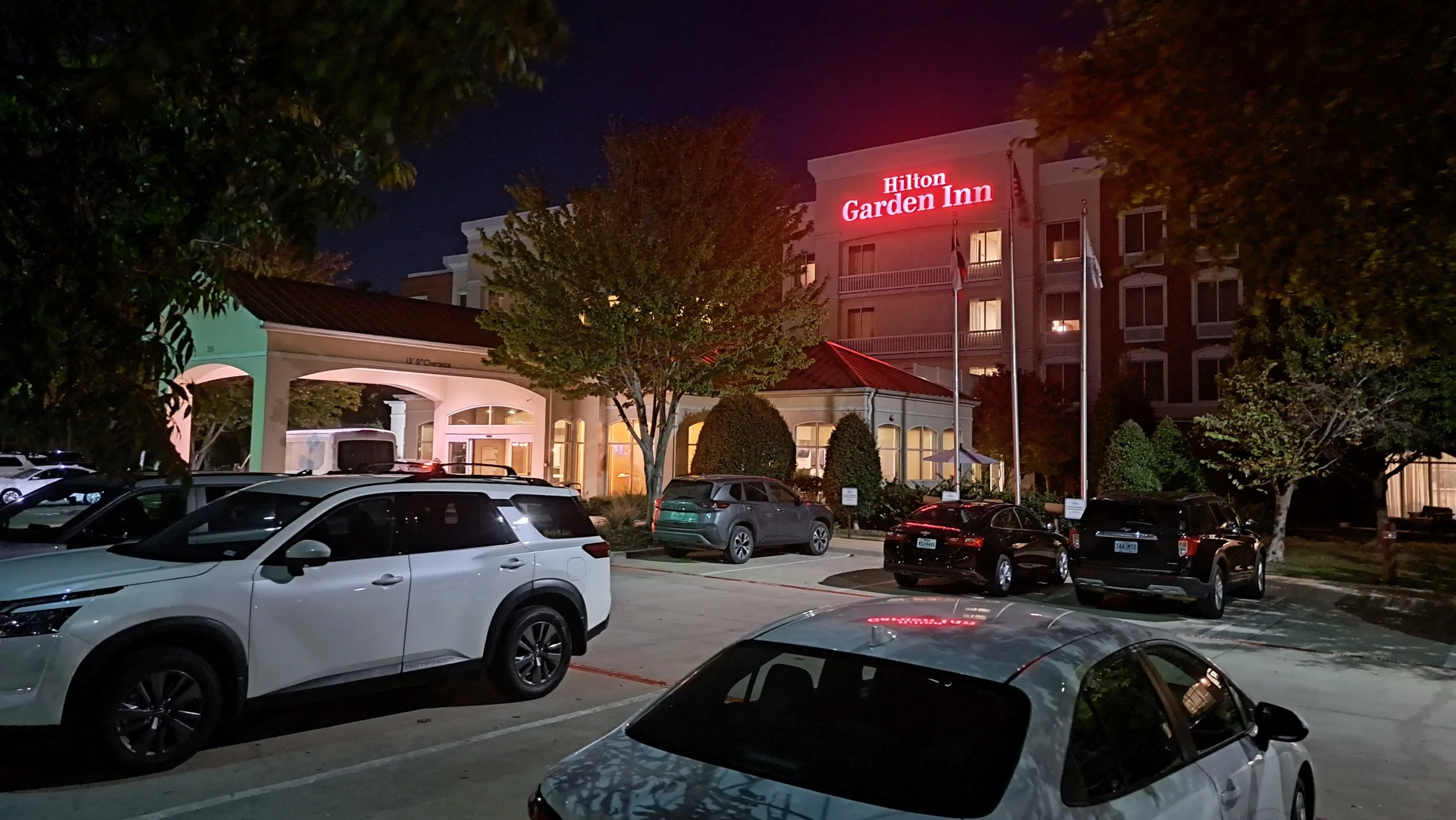 Hilton Garden Inn am Abend mit Parkplatz und Bäumen