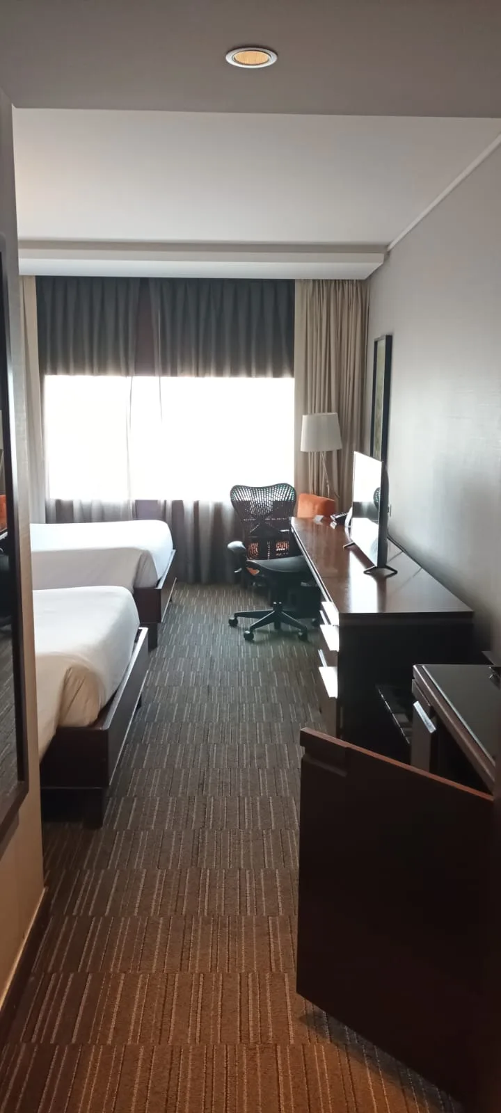 Hotelzimmer mit Doppelbetten und Schreibtisch in neutralen Farben