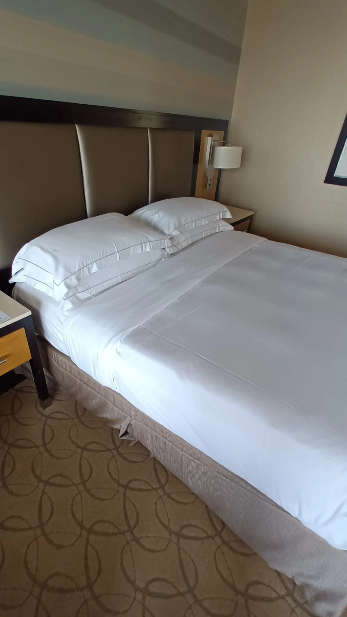 Doppelbett im Hotelzimmer mit grauem Kopfteil und Tagesdecke