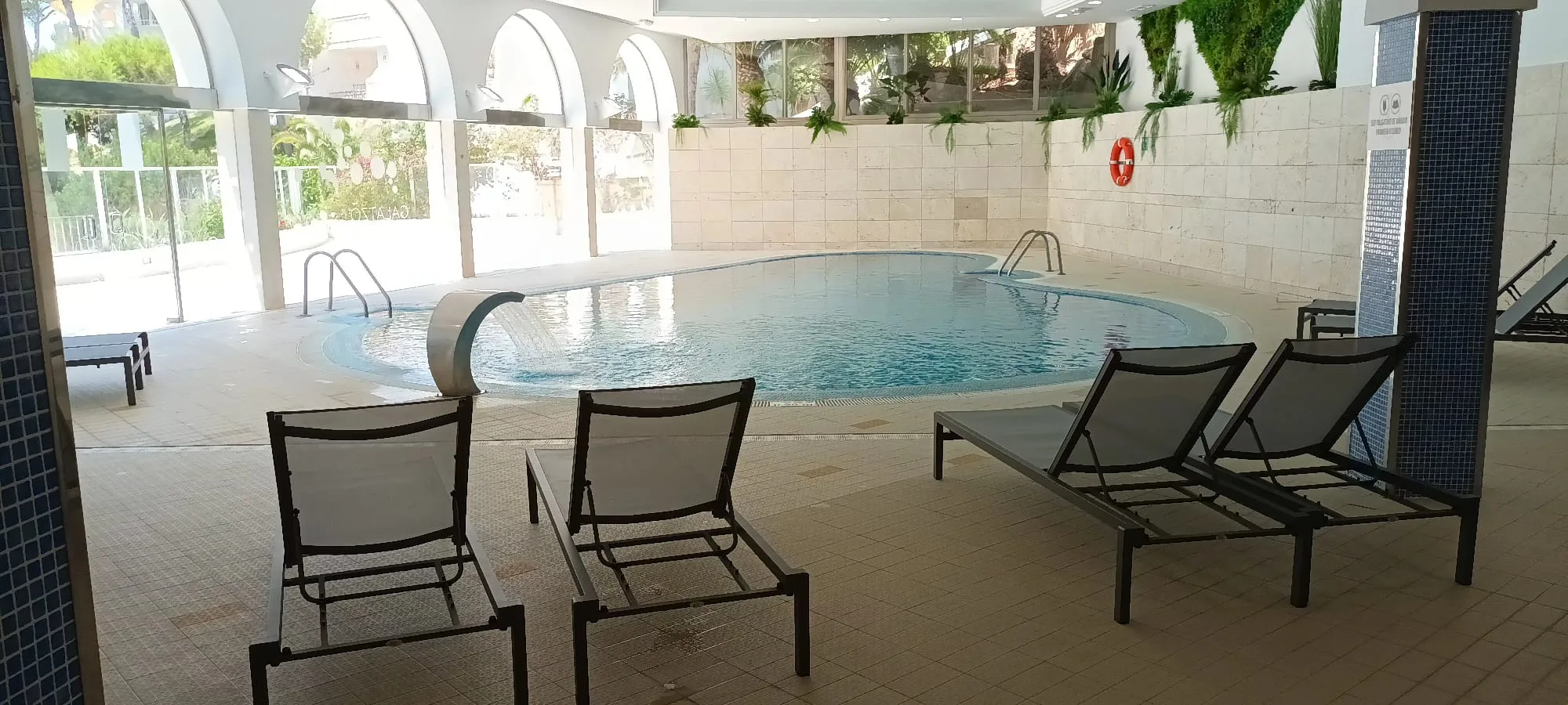 Indoor Pool mit Liegestühlen und Wasserfall im Hintergrund
