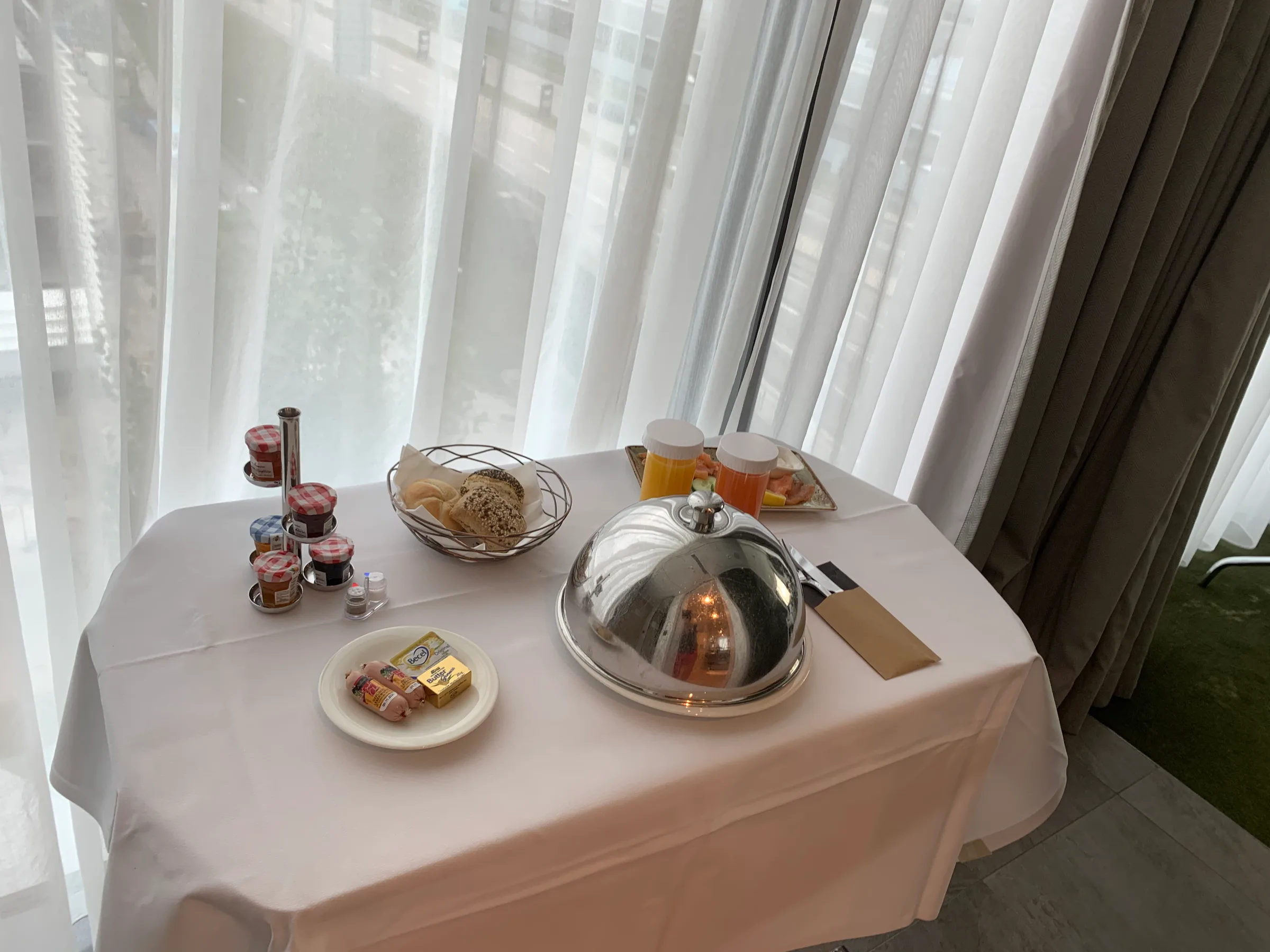 Frühstückstablett mit Brot, Marmeladen und Getränken auf weißer Tischdecke