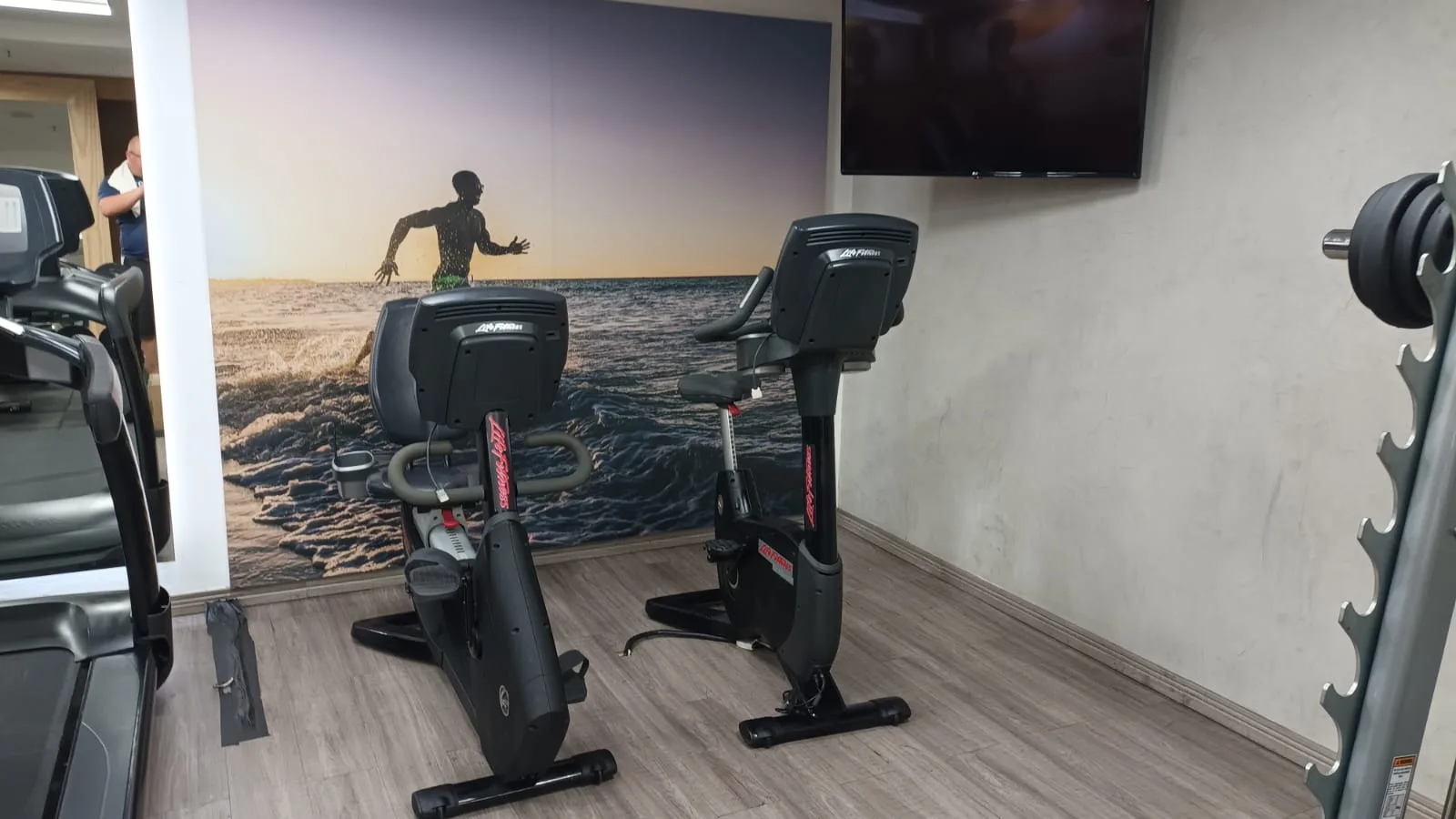 Fitnessraum mit Laufband, Fahrrädern und Wandbild