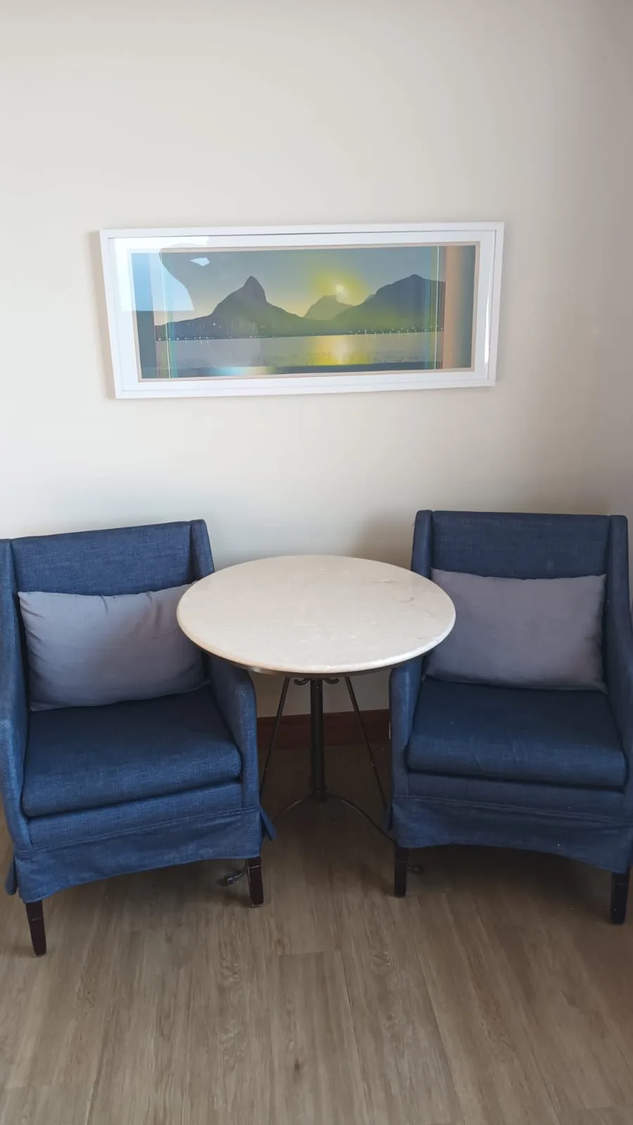 Zwei blaue Sessel und ein runder Tisch vor einer Landschaftsaufnahme an der Wand